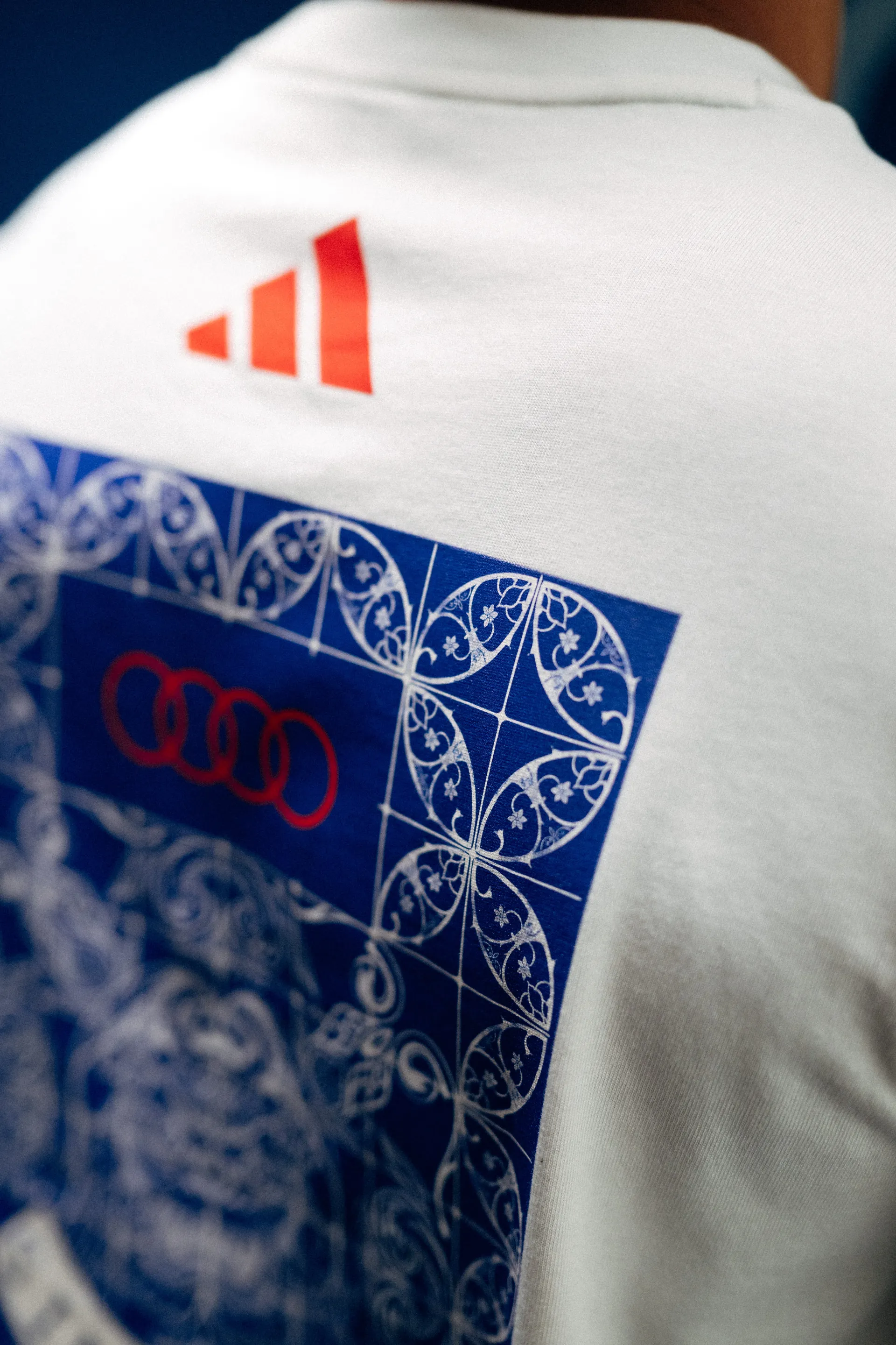 Close-up of a white Audi Revolut F1® Team tee shoulder with tile-pattern print and adidas logo