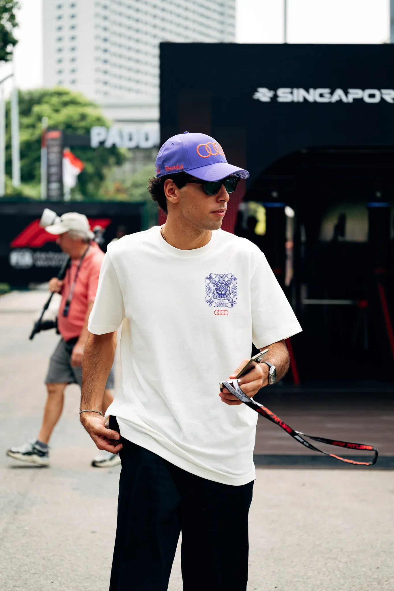 Gabriel Bortoleto, driver of the Audi Revolut F1® Team, walking through the Singapore paddock in a white T-shirt and cap.