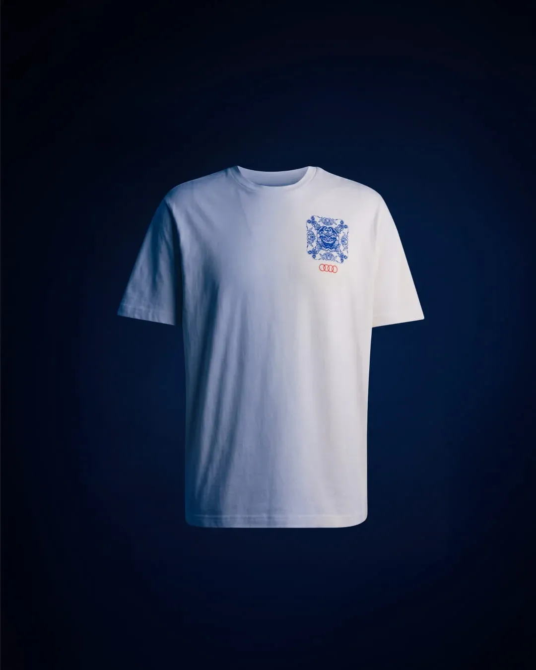 White t-shirt with small blue ornamental badge and Audi rings on the chest