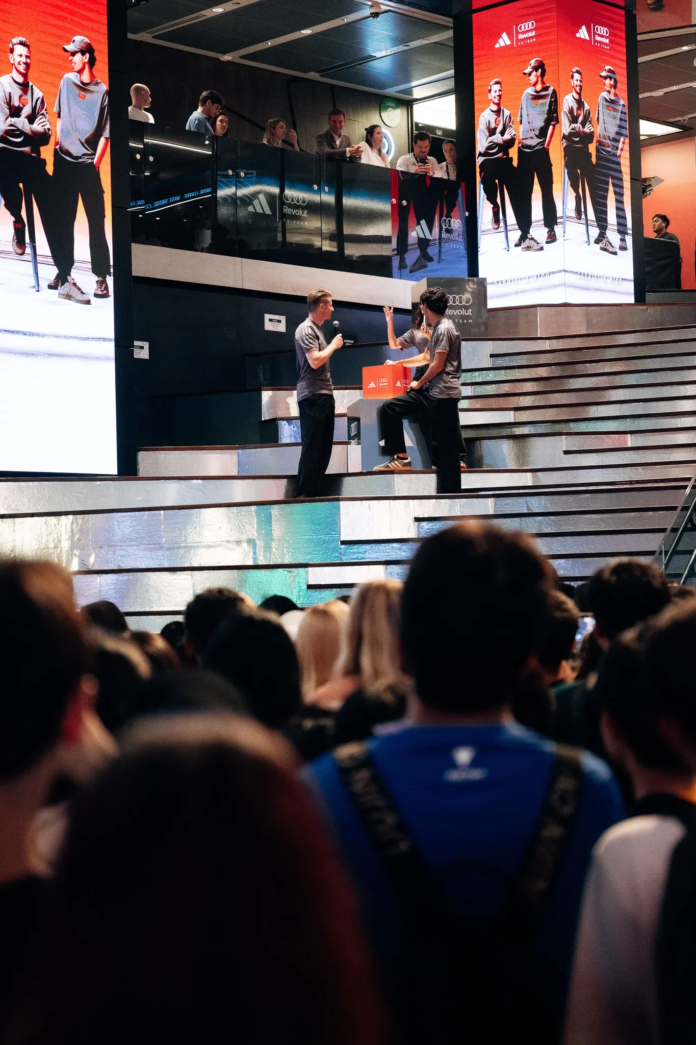 Audience watching a live presentation on a large indoor stage.