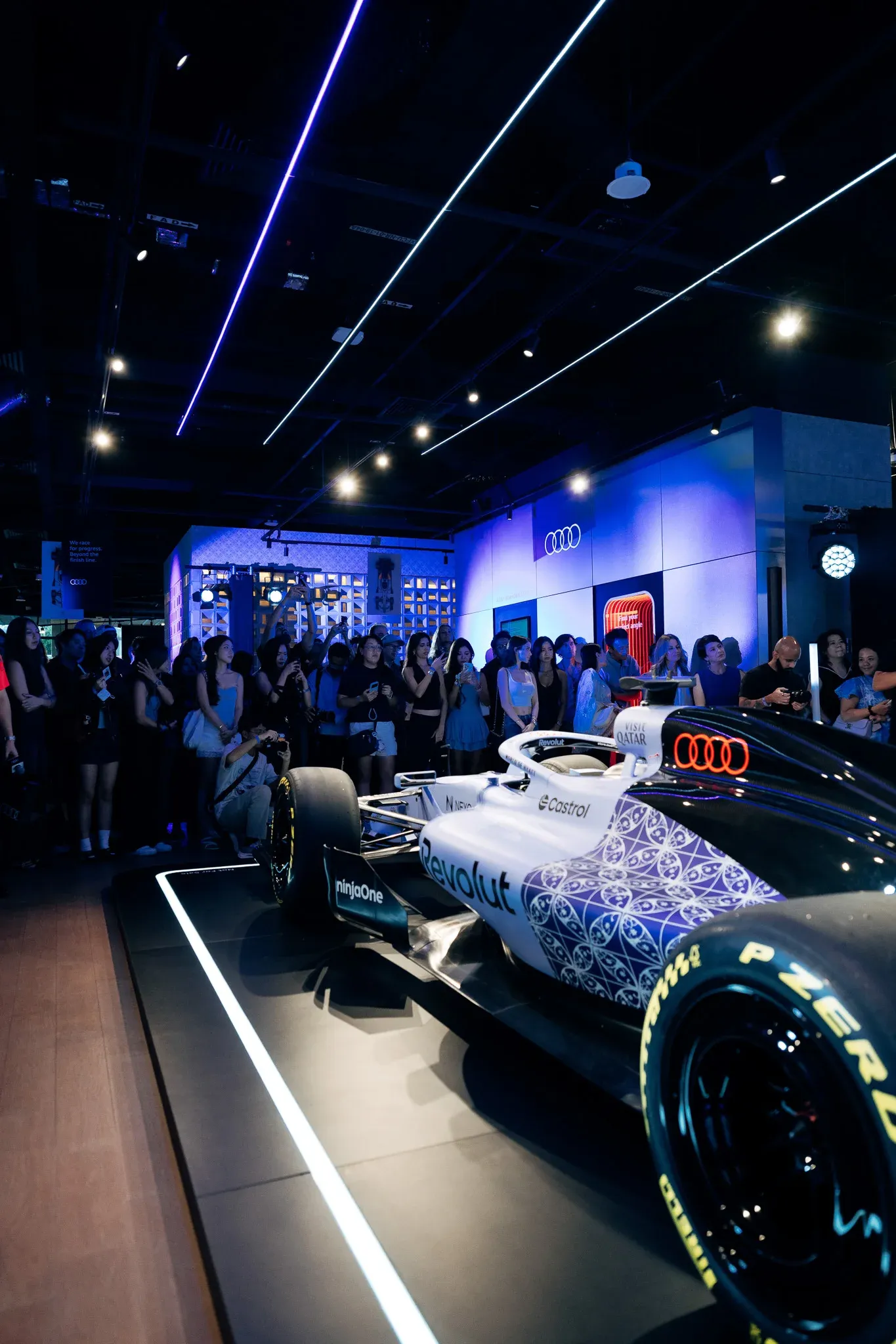 Audi Revolut F1® Team car R26 displayed at an indoor event with blue lighting and spectators.