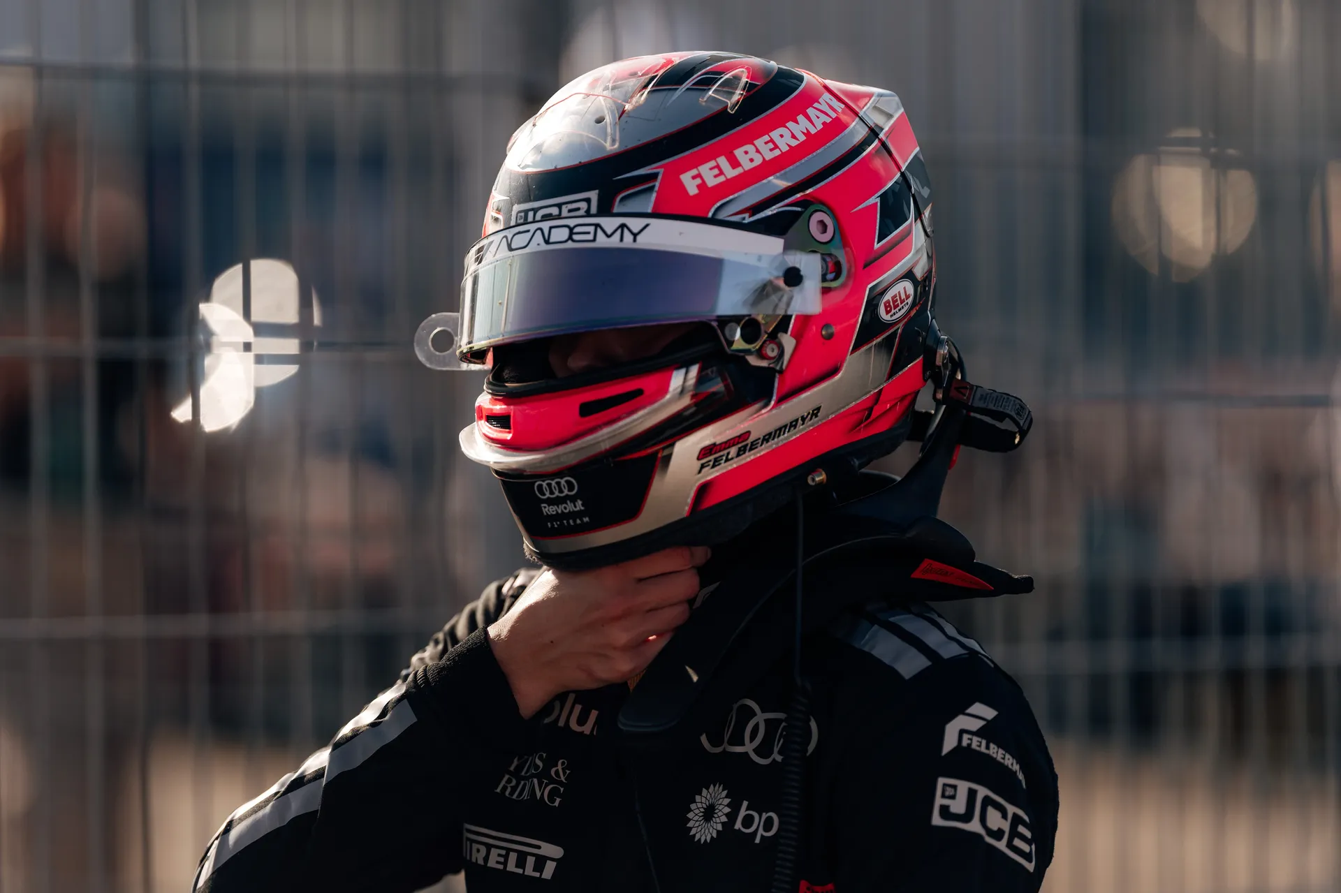 Emma Felbermayr stands in her race suit adjusting her helmet strap ahead of an F1 Academy session at Silverstone.