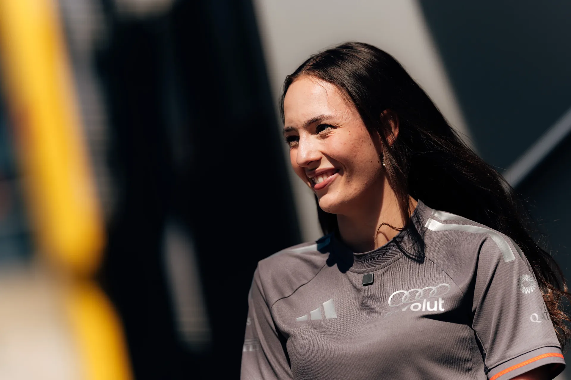 Carrie Schreiner, mentor in the Audi driver development programme, smiles in team apparel while interacting in the paddock at Silverstone.