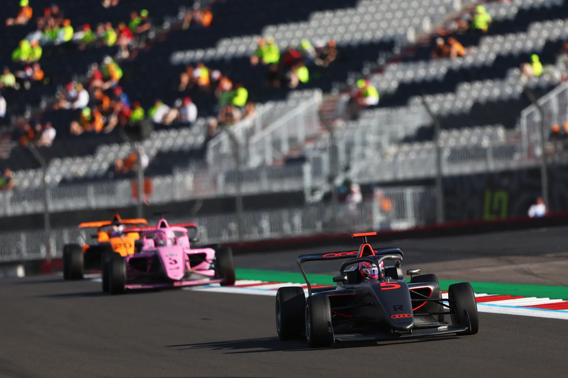 Audi Revolut F1® Team F1 Academy car #5 leads a group of cars through a corner at Silverstone with grandstands in the background.