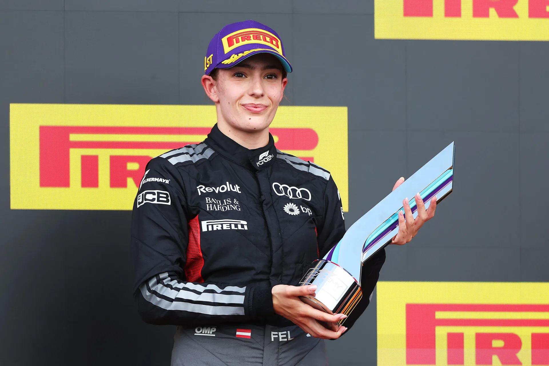 Emma Felbermayr stands on the podium wearing an Audi Revolut F1® Team race suit and Pirelli cap, holding a trophy after a strong result in F1 Academy.