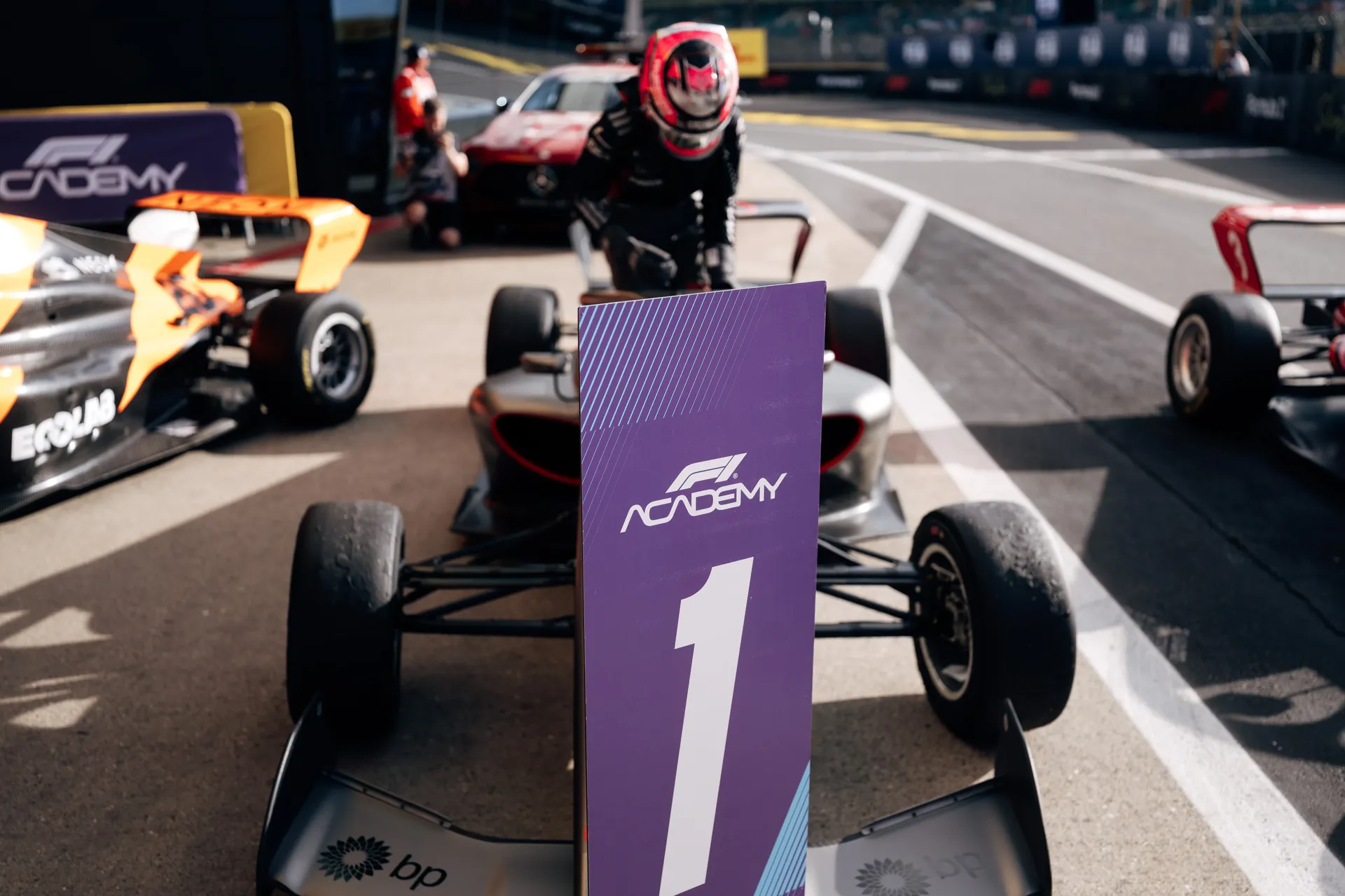 F1 Academy car of the Audi Revolut F1® Team is parked in the pit lane at Silverstone with a large P1 position board in the foreground, while a driver in full race gear stands behind the car.