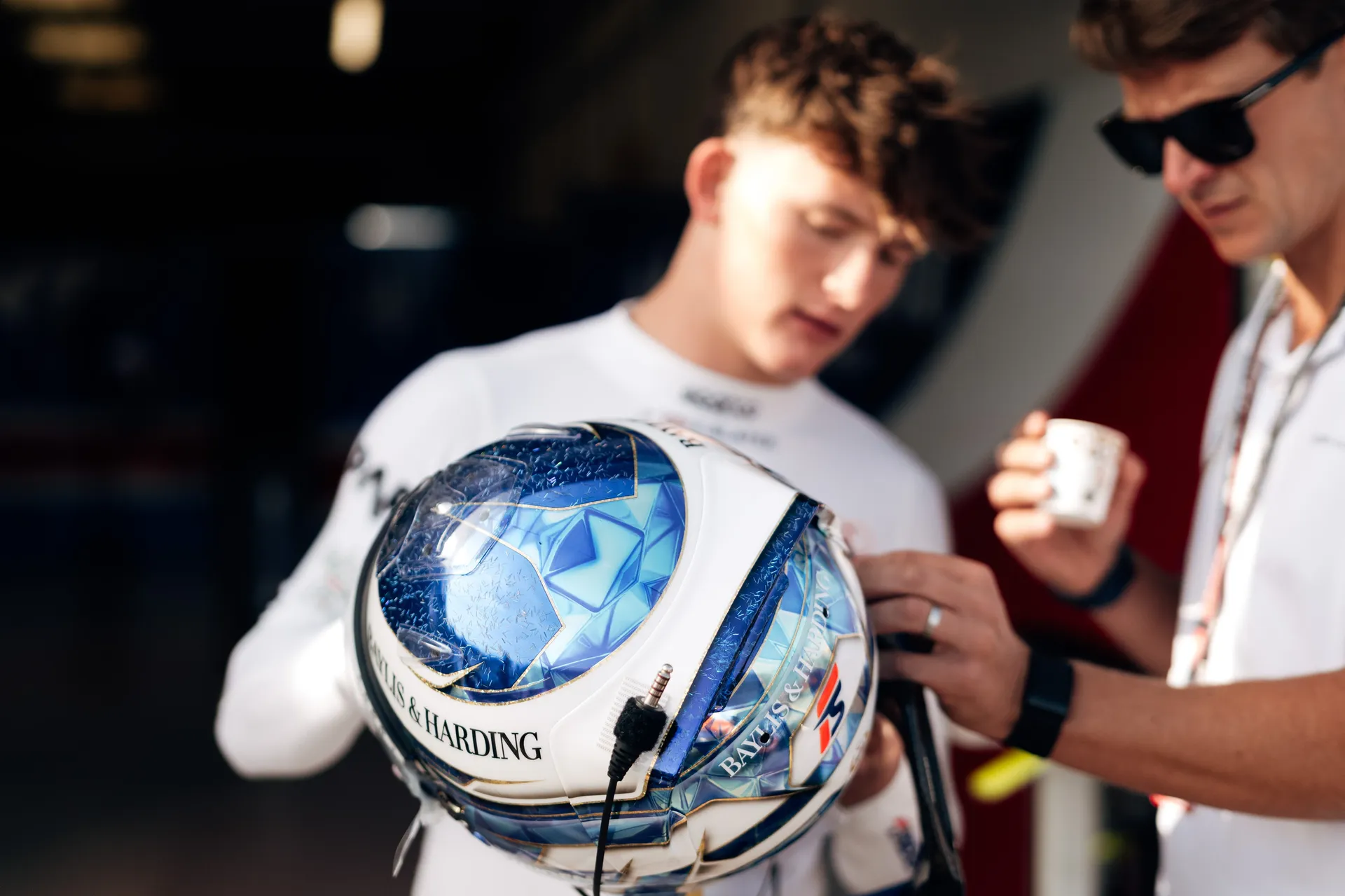 Freddie Slater inspects his helmet with a team member in the garage, preparing for an F3 session alongside Audi driver development programme activities at Silverstone.