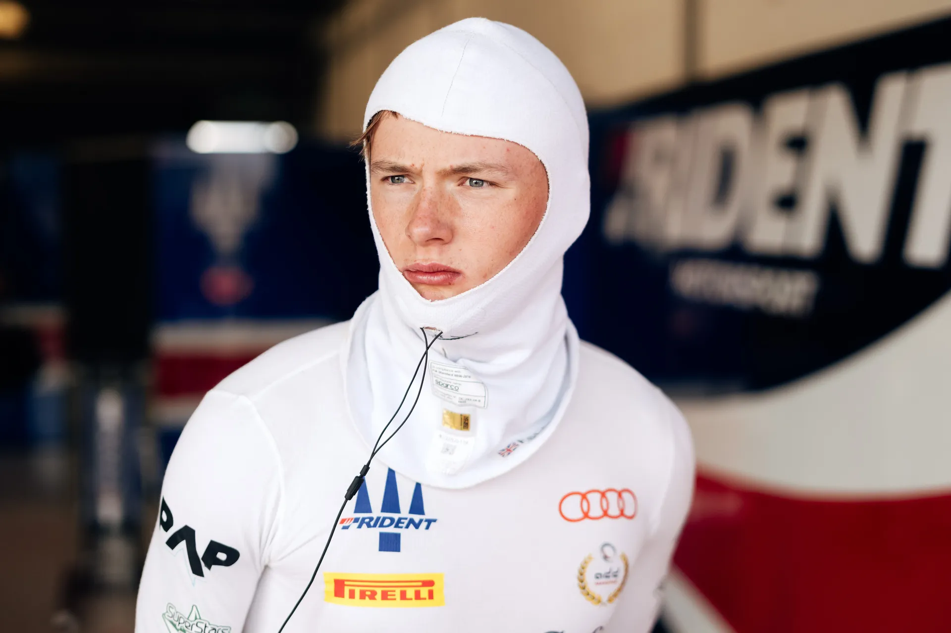 Freddie Slater wearing a white balaclava and race underwear, focused and looking ahead while preparing for his F3 session in the garage.