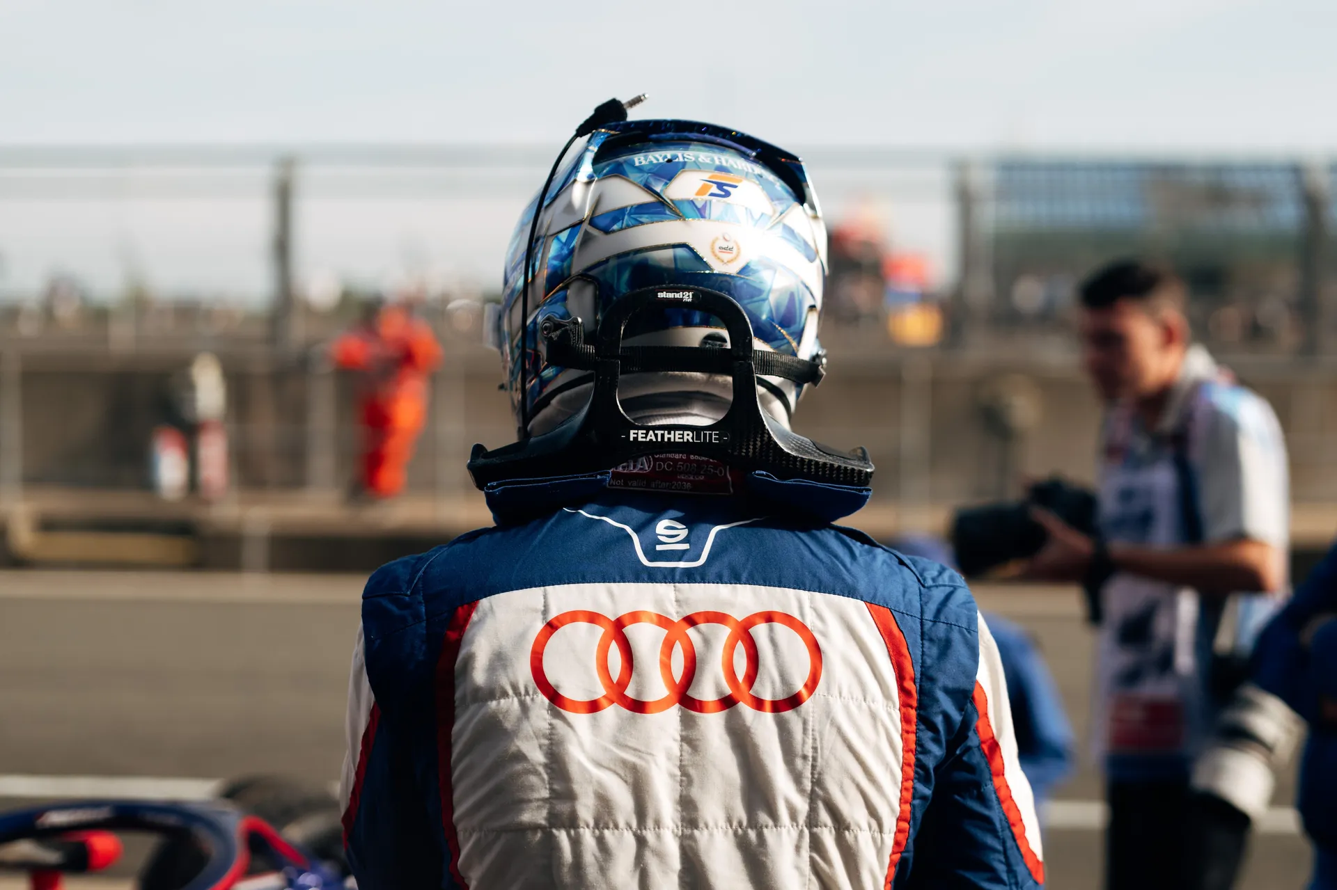 Rear view of Freddie Slater in race suit and helmet standing trackside, Audi rings visible on his back during F3 grid preparations at Silverstone.