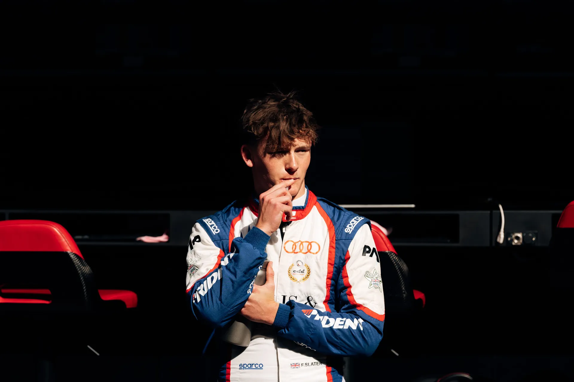 Freddie Slater in race suit stands in the garage, holding a bottle and looking thoughtful ahead of his F3 outing at Silverstone.