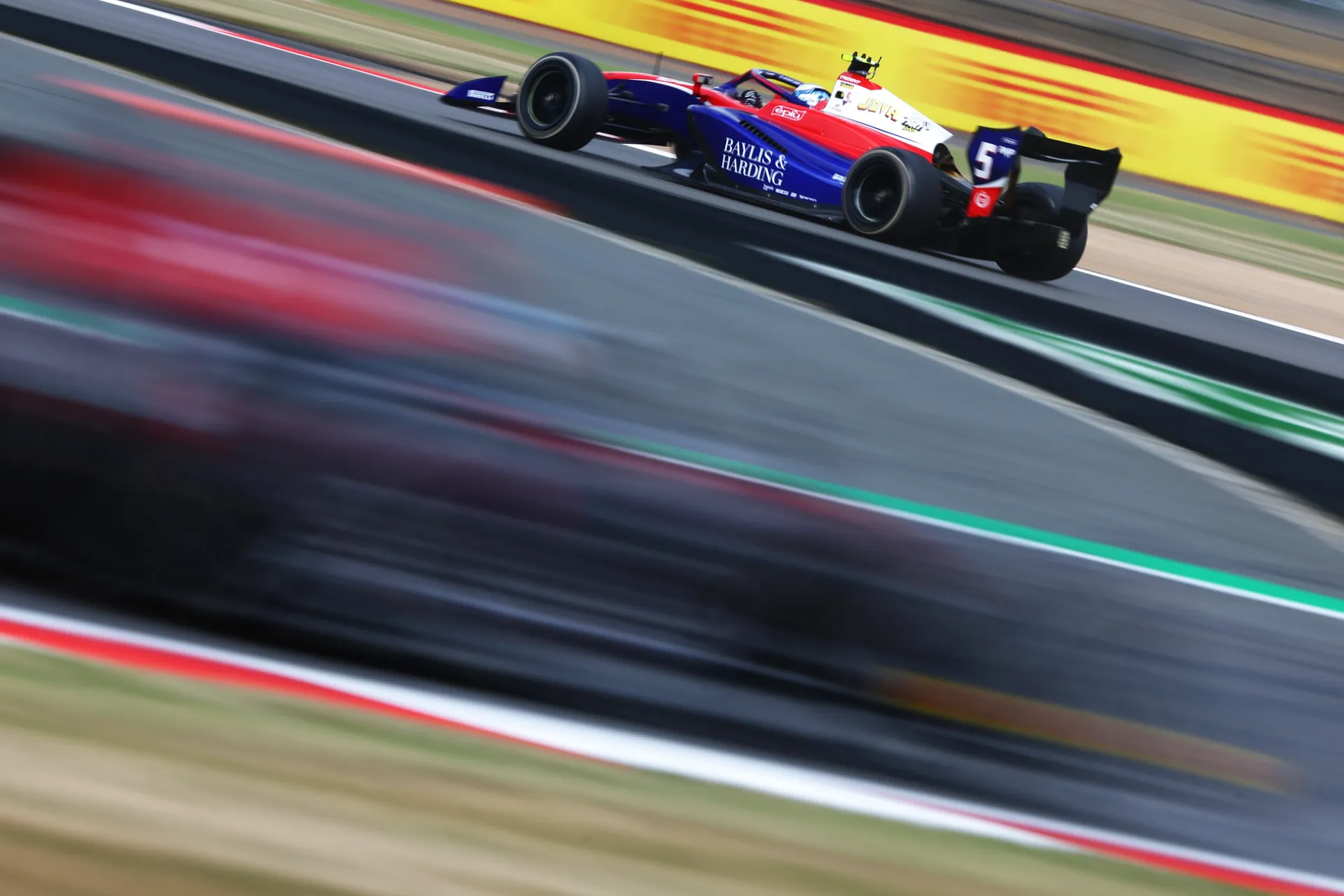 Freddie Slater in a Trident Formula 3 car at speed on track, captured with motion blur as he accelerates through a section of the Silverstone circuit.