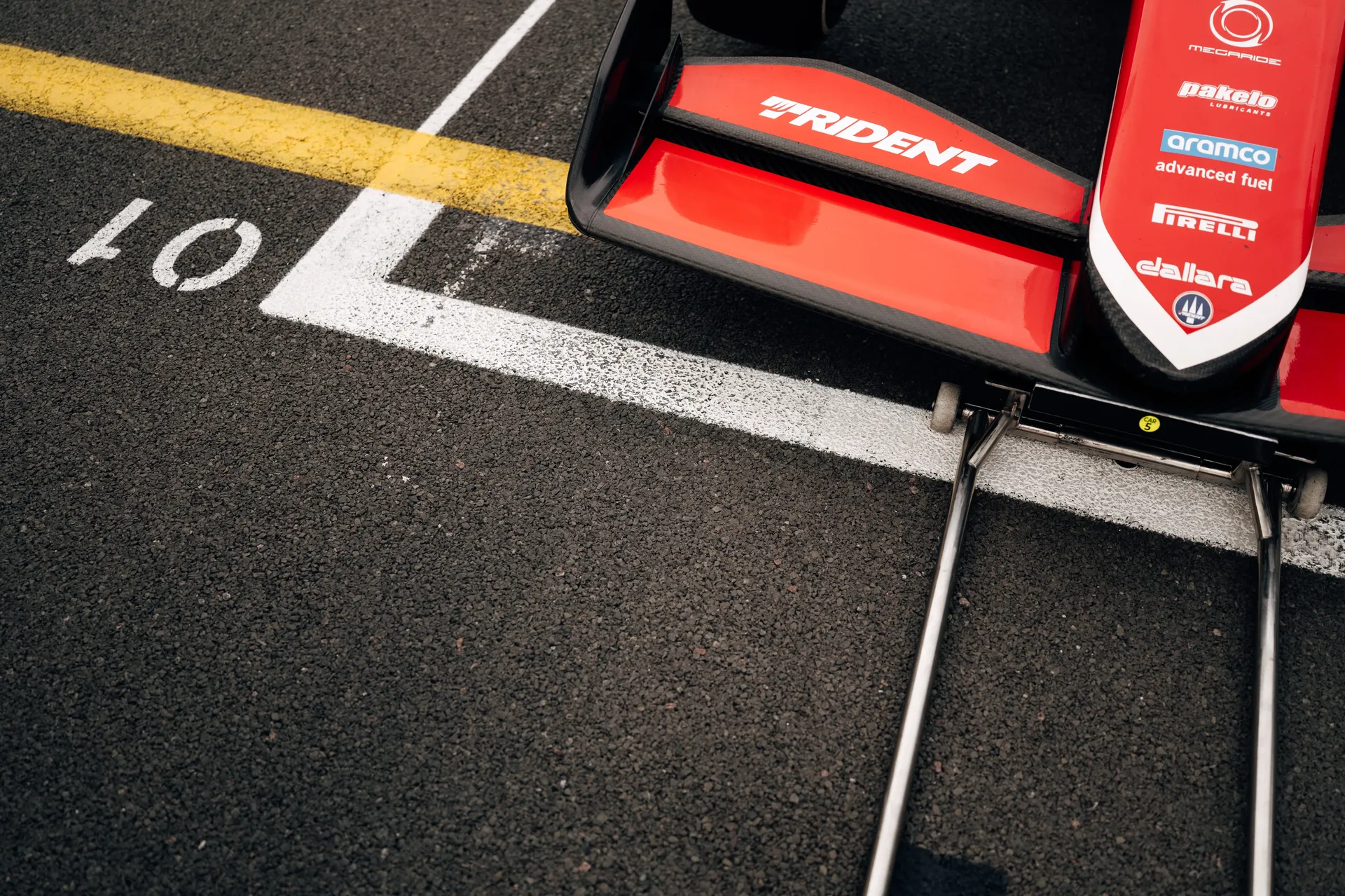 Detail of the front wing and nose of a Trident Formula 3 car positioned on the grid at Silverstone, showing sponsor logos and grid markings on the track surface.