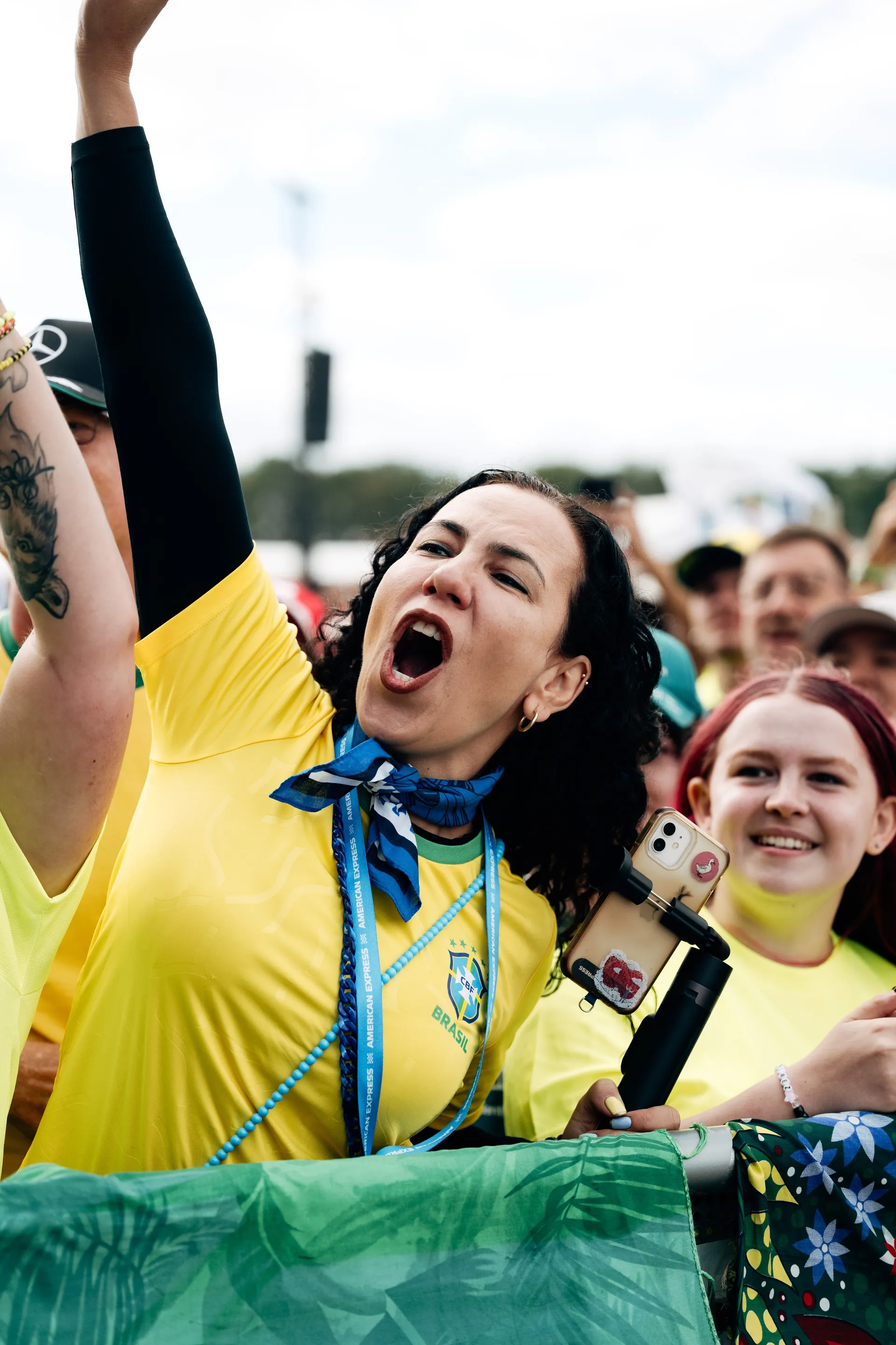 A fan in a Brazil shirt cheers with her arm raised while holding a phone on a stabiliser in the crowd at the Audi Revolut F1® Team fan forum.