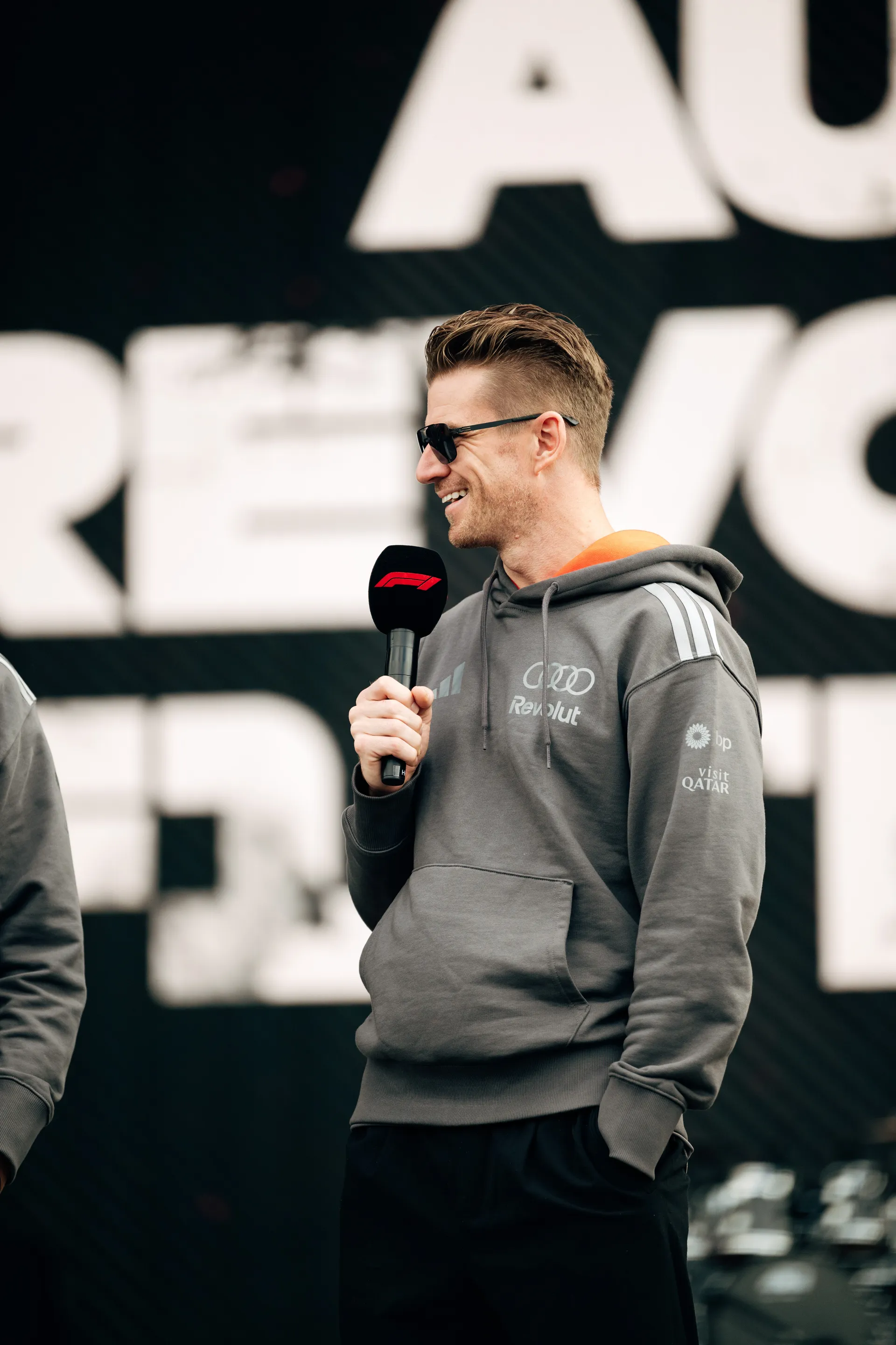 Nico Hulkenberg speaks into a microphone on stage wearing Audi Revolut F1® Team gear during the fan forum.