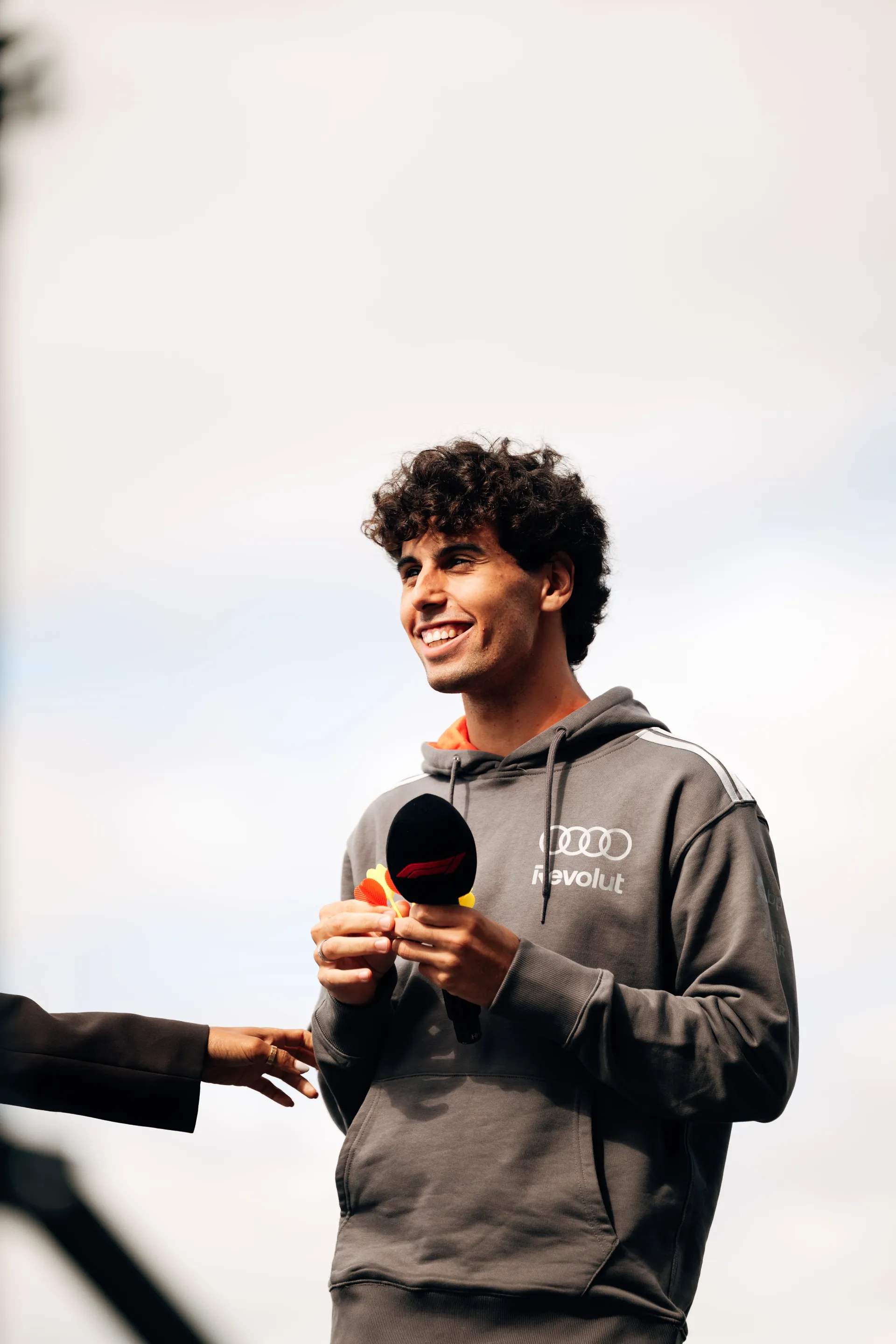 Gabriel Bortoleto stands on stage holding a microphone and smiling during the Audi Revolut F1® Team fan forum.