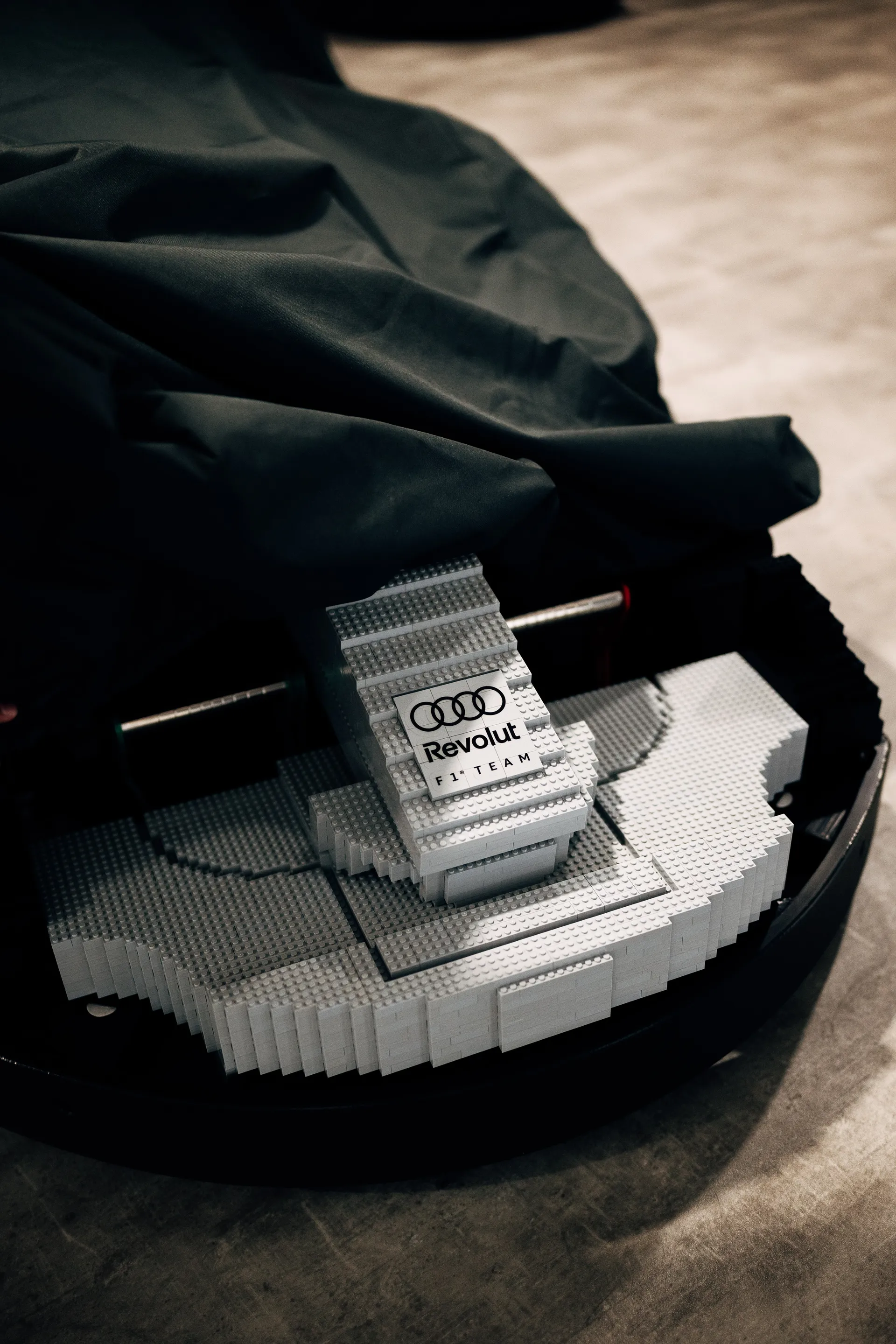 Audi Revolut F1® Team member lifting a cover to reveal a LEGO-built kart, showing the branded front section.
