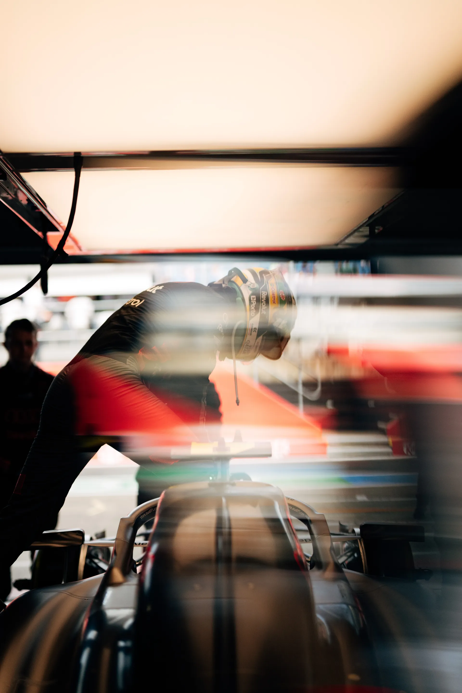 Gabriel Bortoleto leans over the Audi R26 cockpit inside the Audi Revolut F1® Team garage, preparing for a Qualifying run under bright overhead lighting.