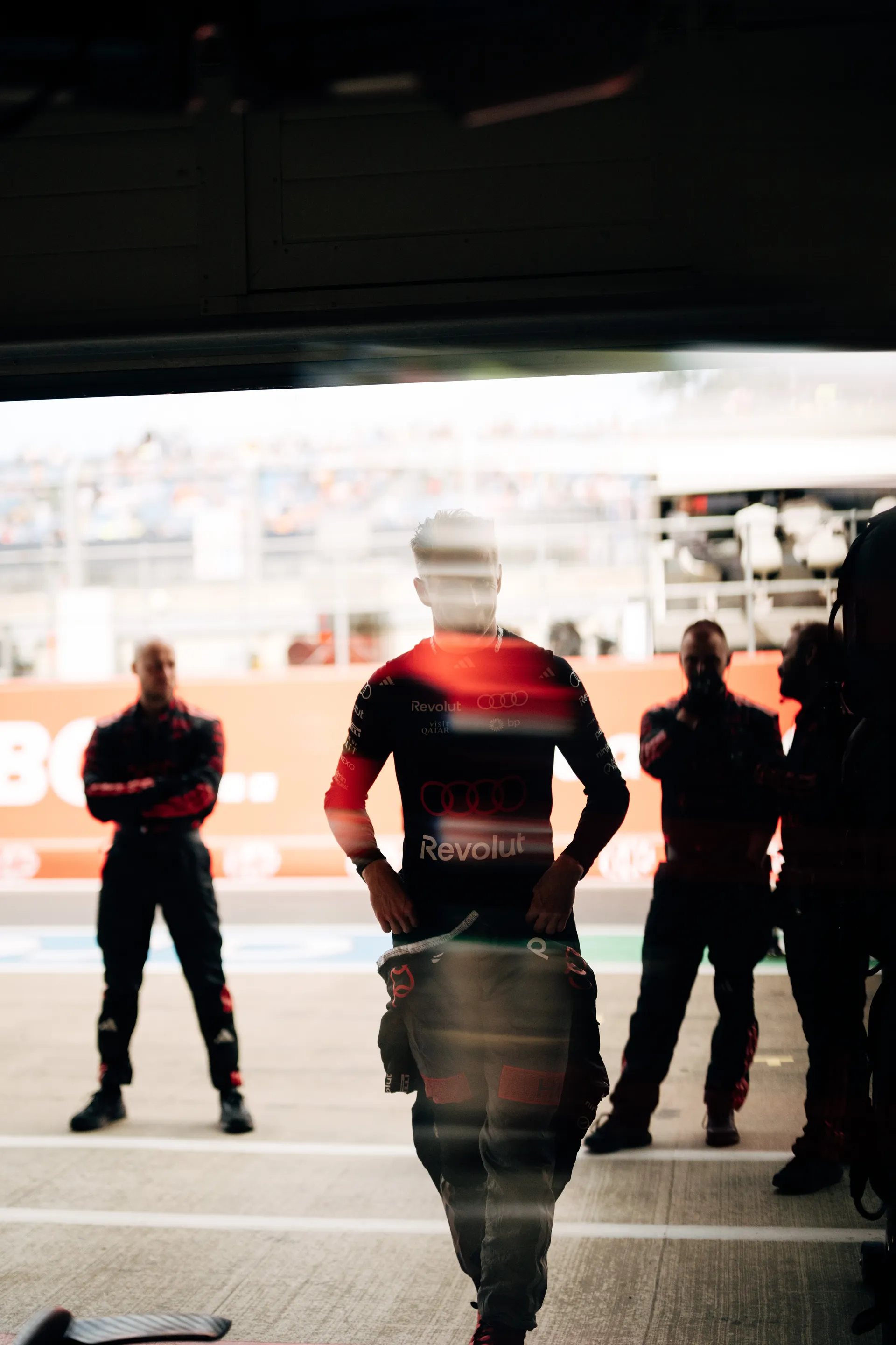 Nico Hulkenberg walks out of the Audi Revolut F1® Team garage towards the pit lane, silhouetted against daylight, with crew members watching ahead of Qualifying.