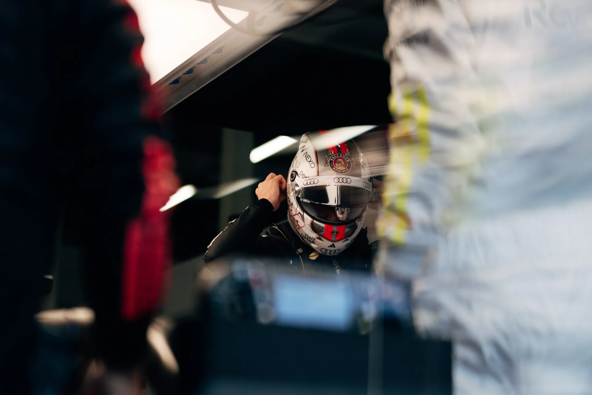 Nico Hulkenberg adjusts his helmet inside the Audi Revolut F1® Team garage, framed by reflections and equipment ahead of Qualifying at Silverstone.