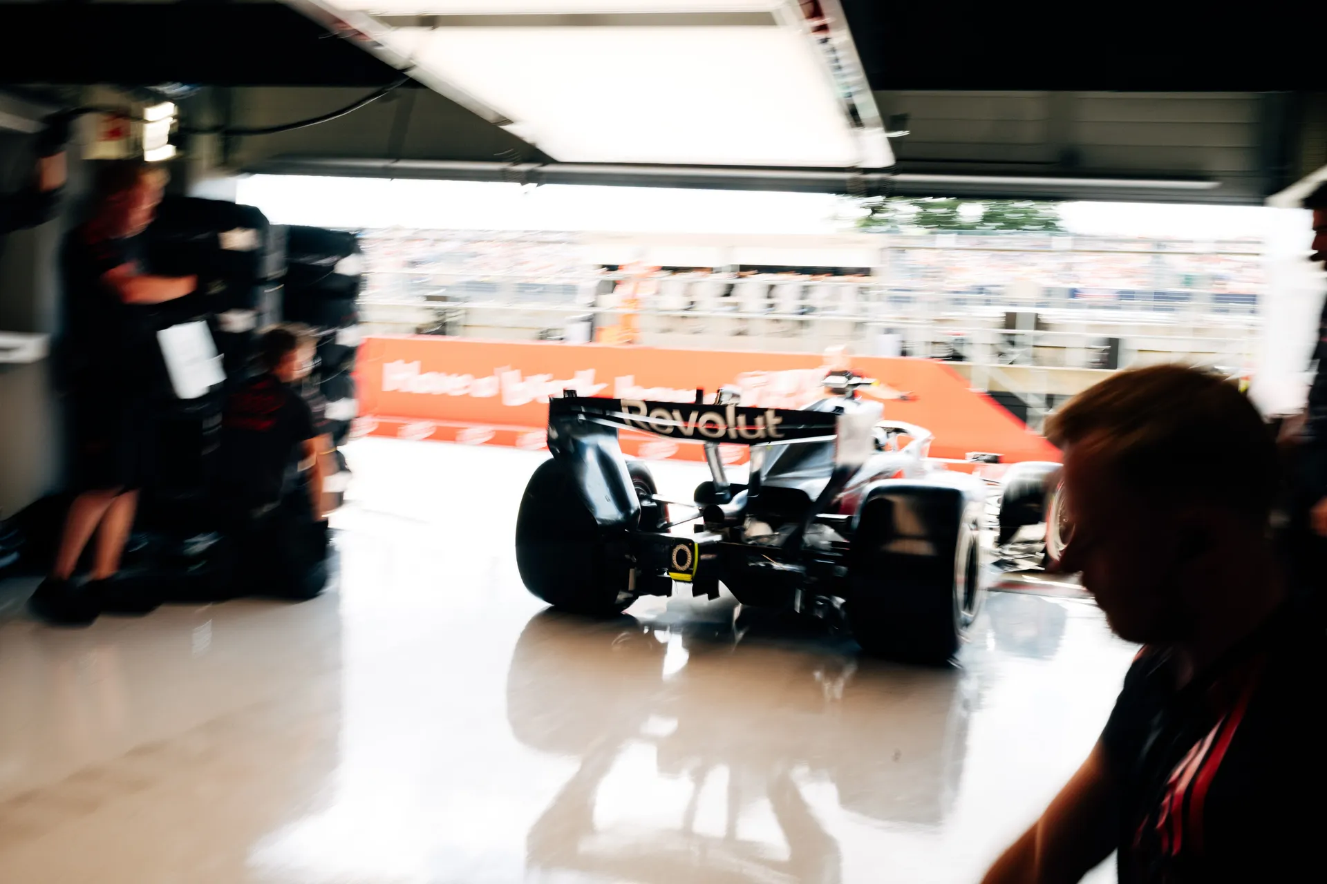 Audi R26 leaving the Audi Revolut F1® Team garage and heading into the pit lane during Qualifying at Silverstone, captured from inside the garage with crew in silhouette.