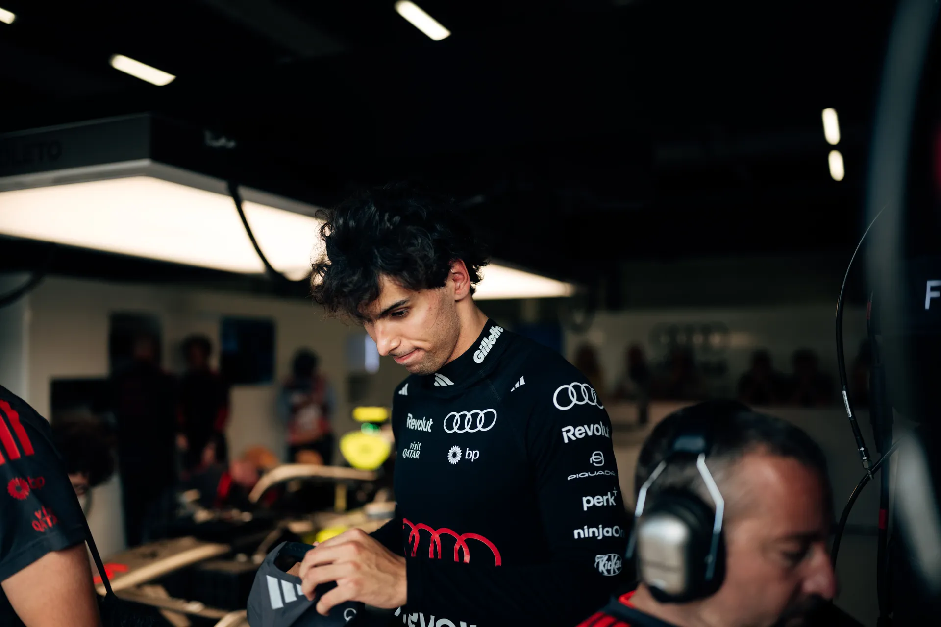 Gabriel Bortoleto wearing his helmet stands inside the Audi Revolut F1® Team garage, fastening his gloves ahead of a Qualifying run at Silverstone.