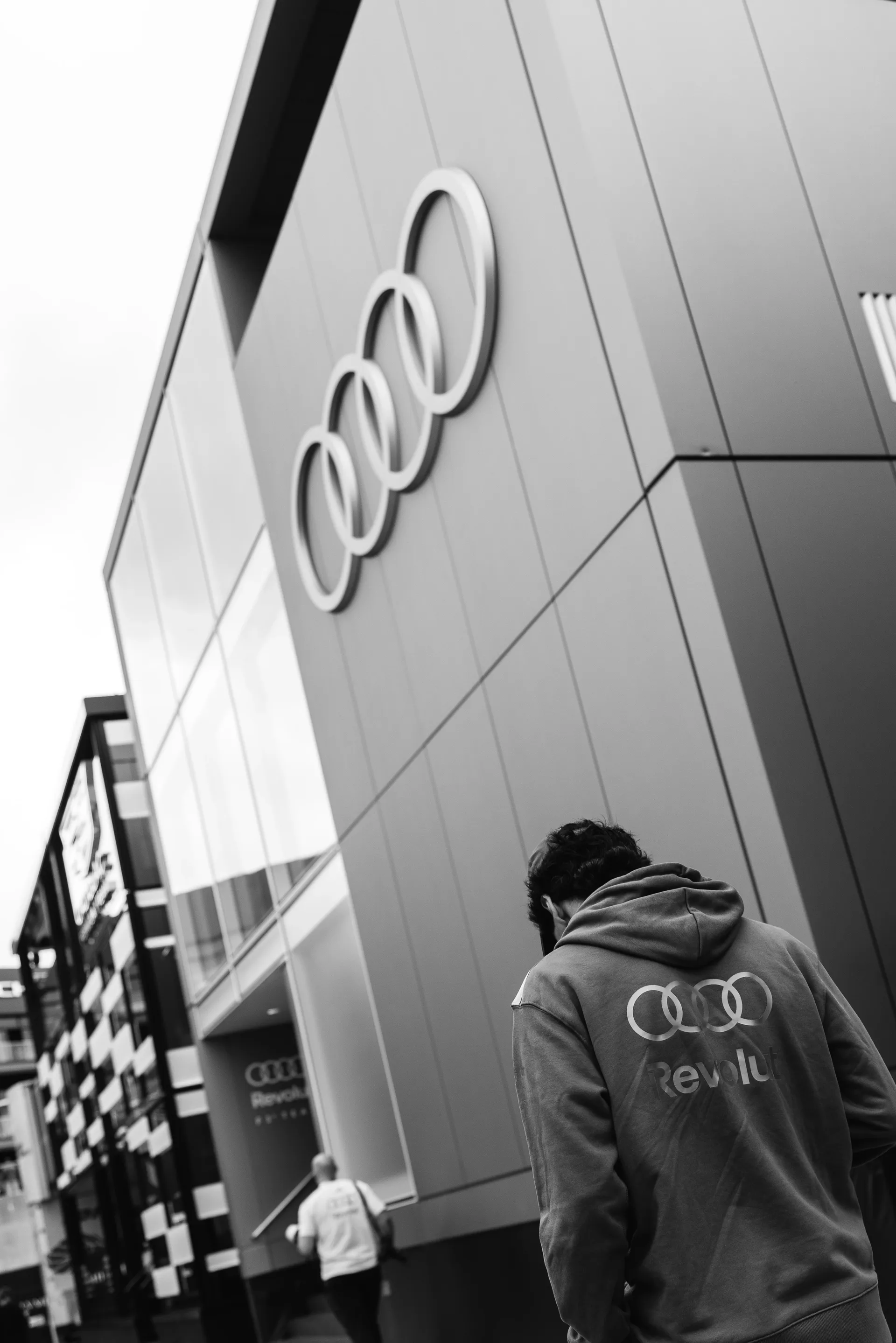 Rear view of Gabriel Bortoleto in Audi Revolut F1® Team hoodie walking past an Audi building with the four rings logo.