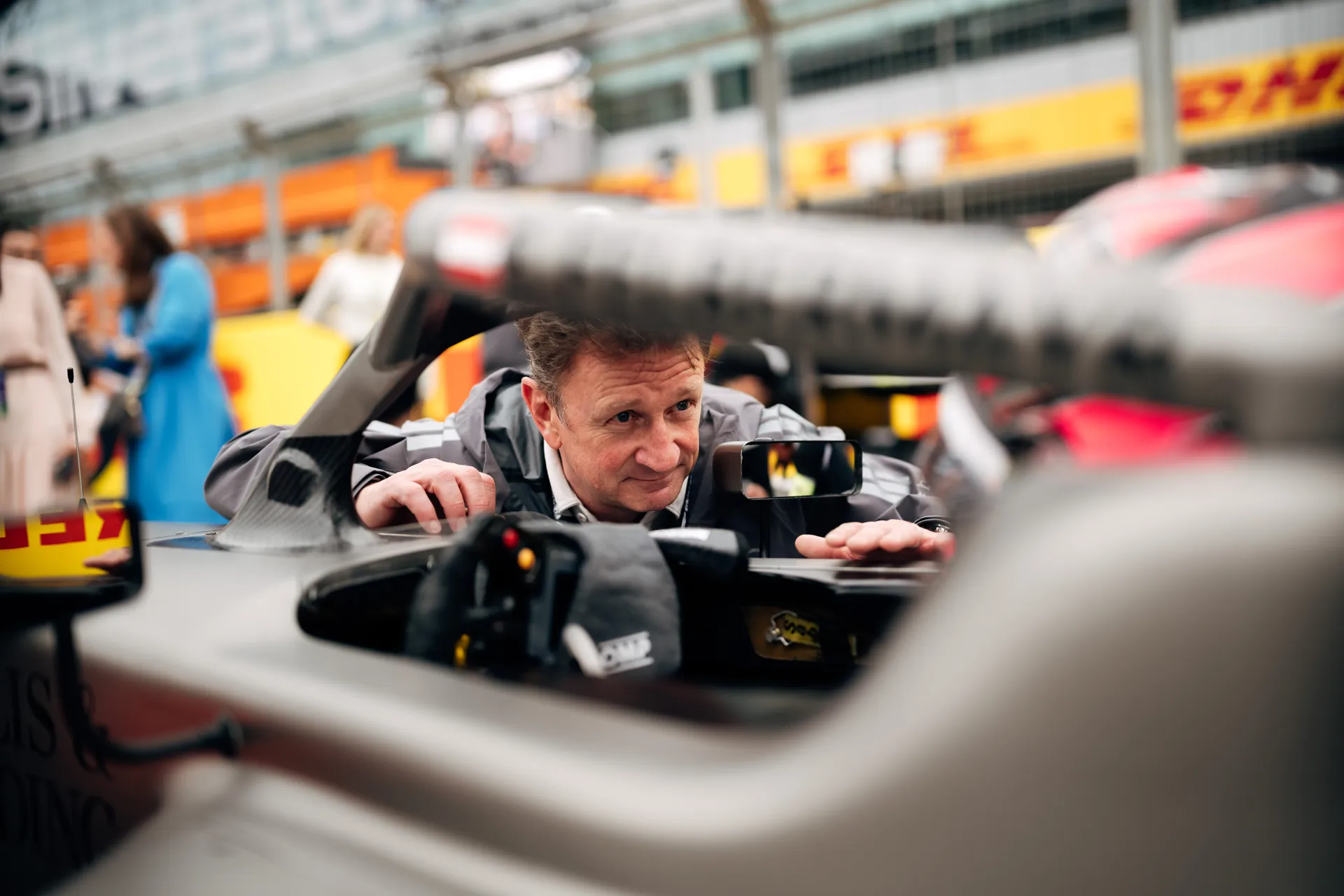 Allan McNish leaning into the cockpit of an Audi Revolut F1® Team car, inspecting details up close.