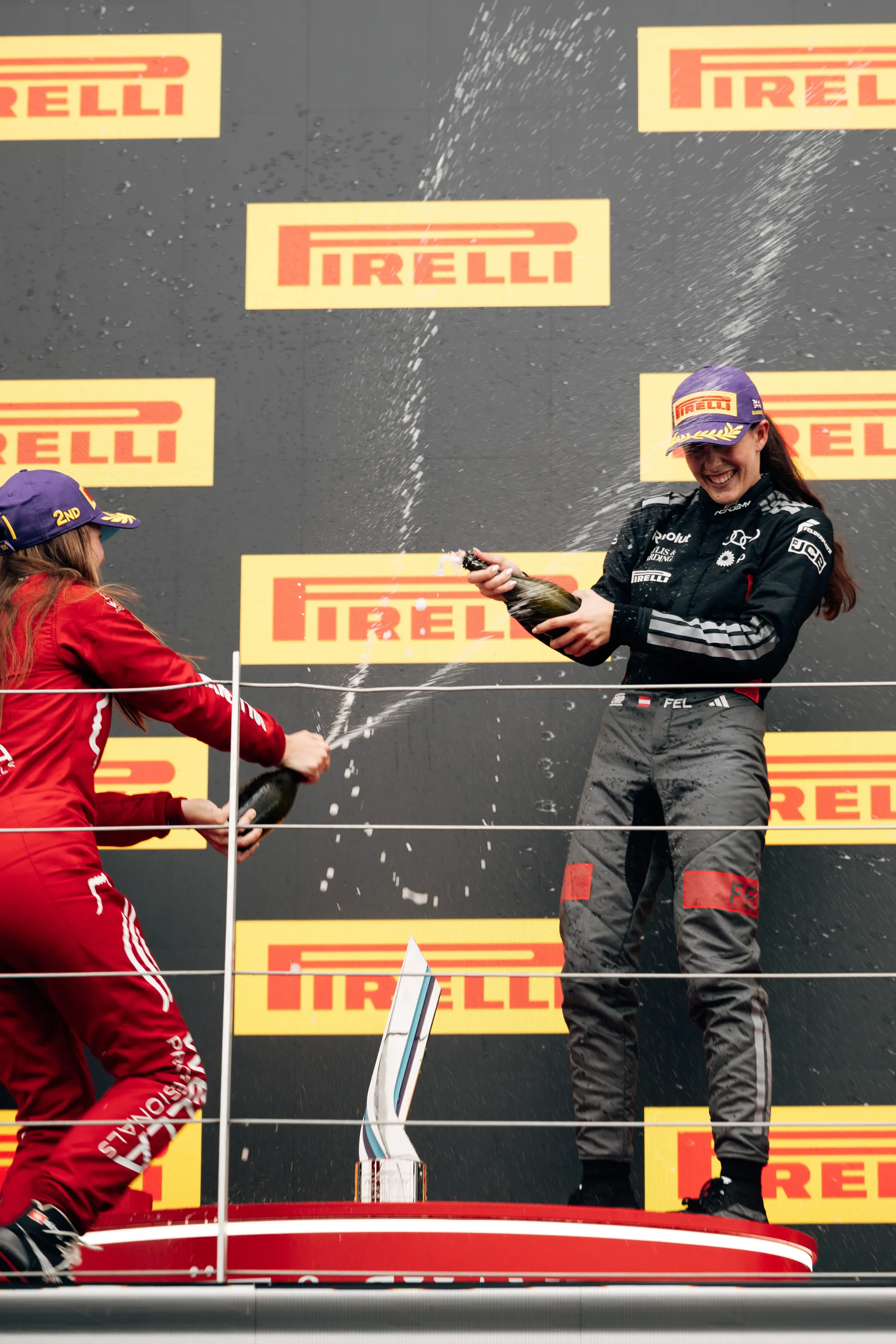 Emma Felbermayr celebrating on the podium, spraying champagne during an F1 Academy ceremony.