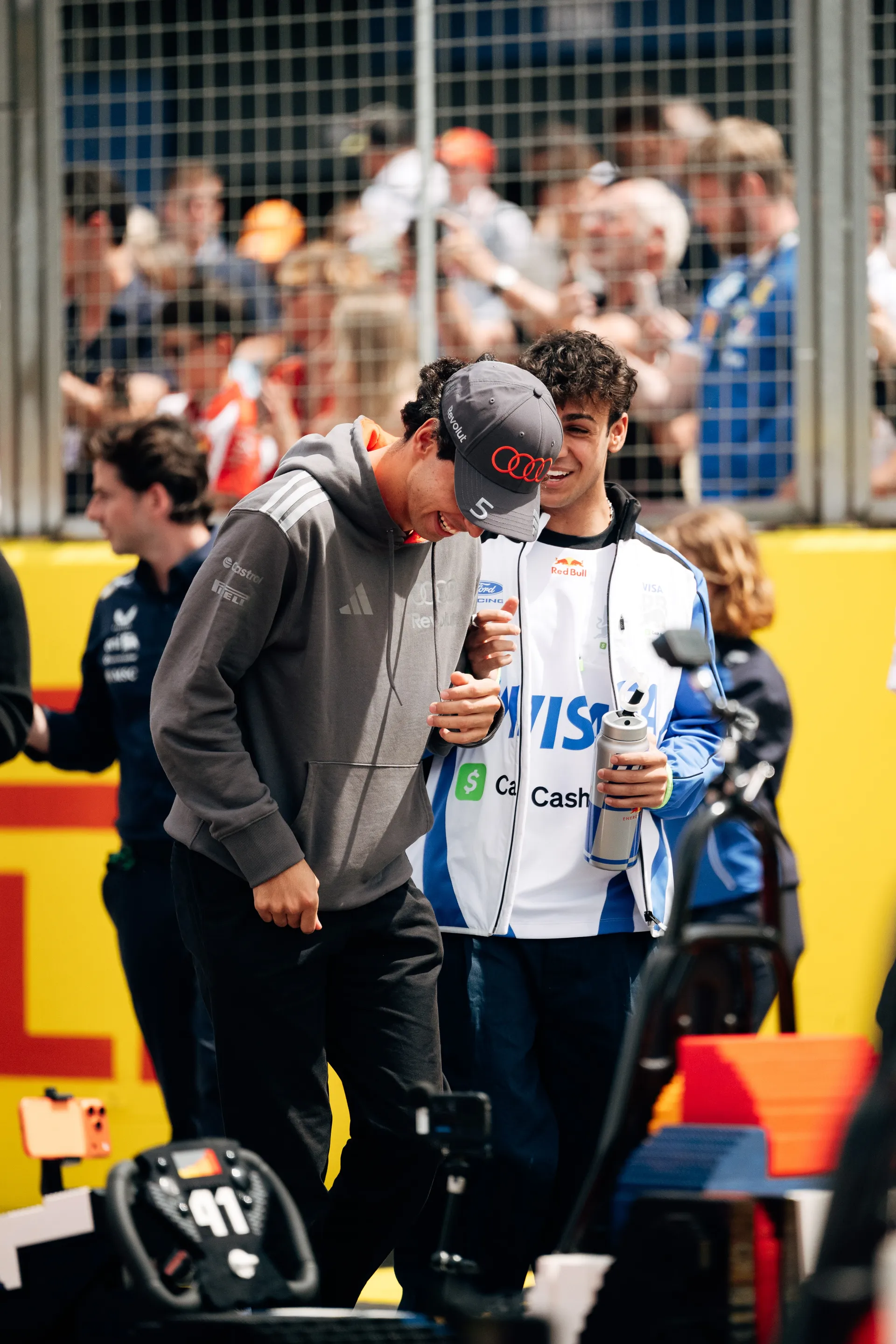 Gabriel Bortoleto laughing with another driver in the paddock in front of spectators.