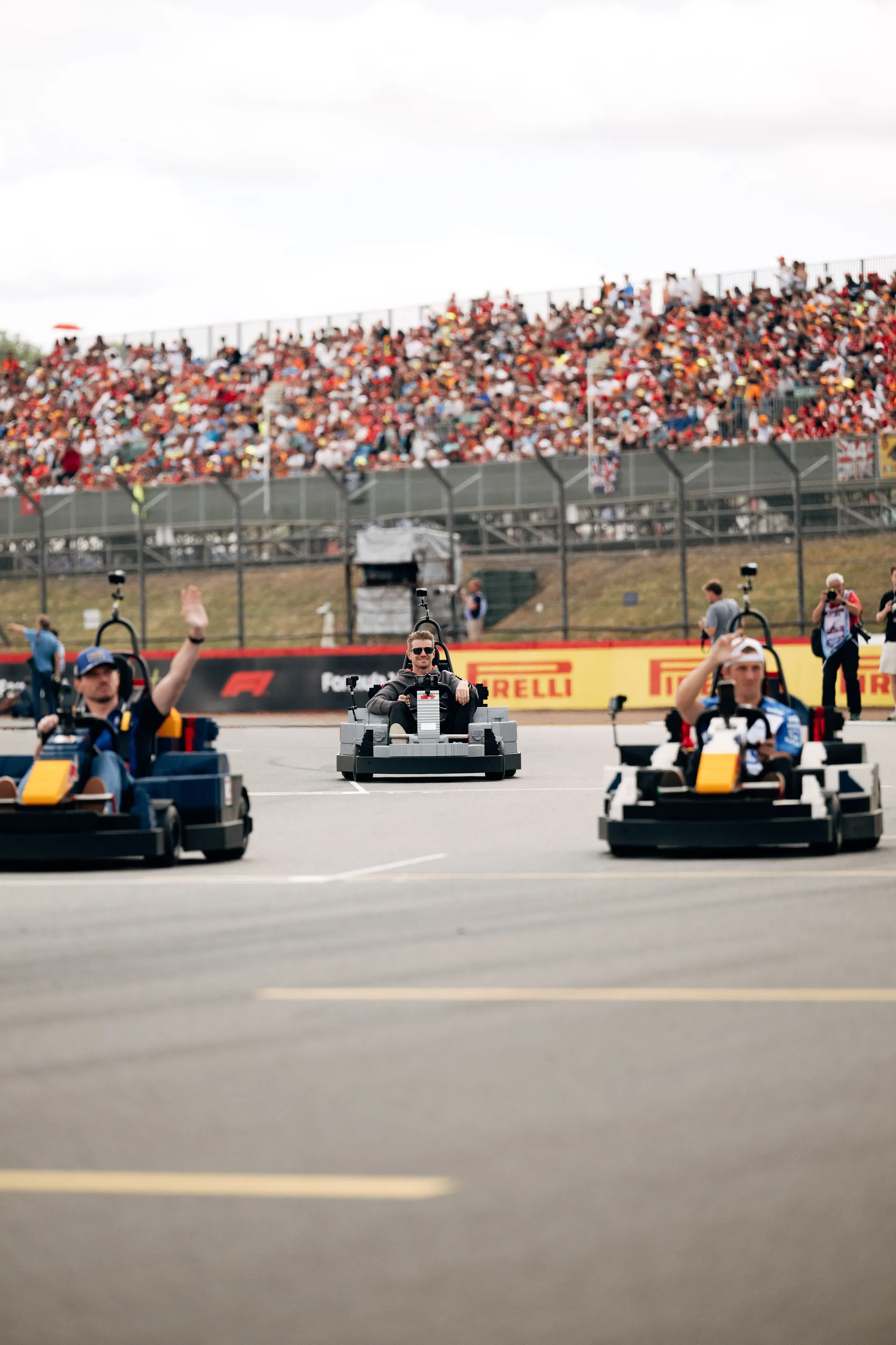 Multiple drivers in LEGO® karts during the Drivers’ Parade at Silverstone, waving to fans in the grandstands.