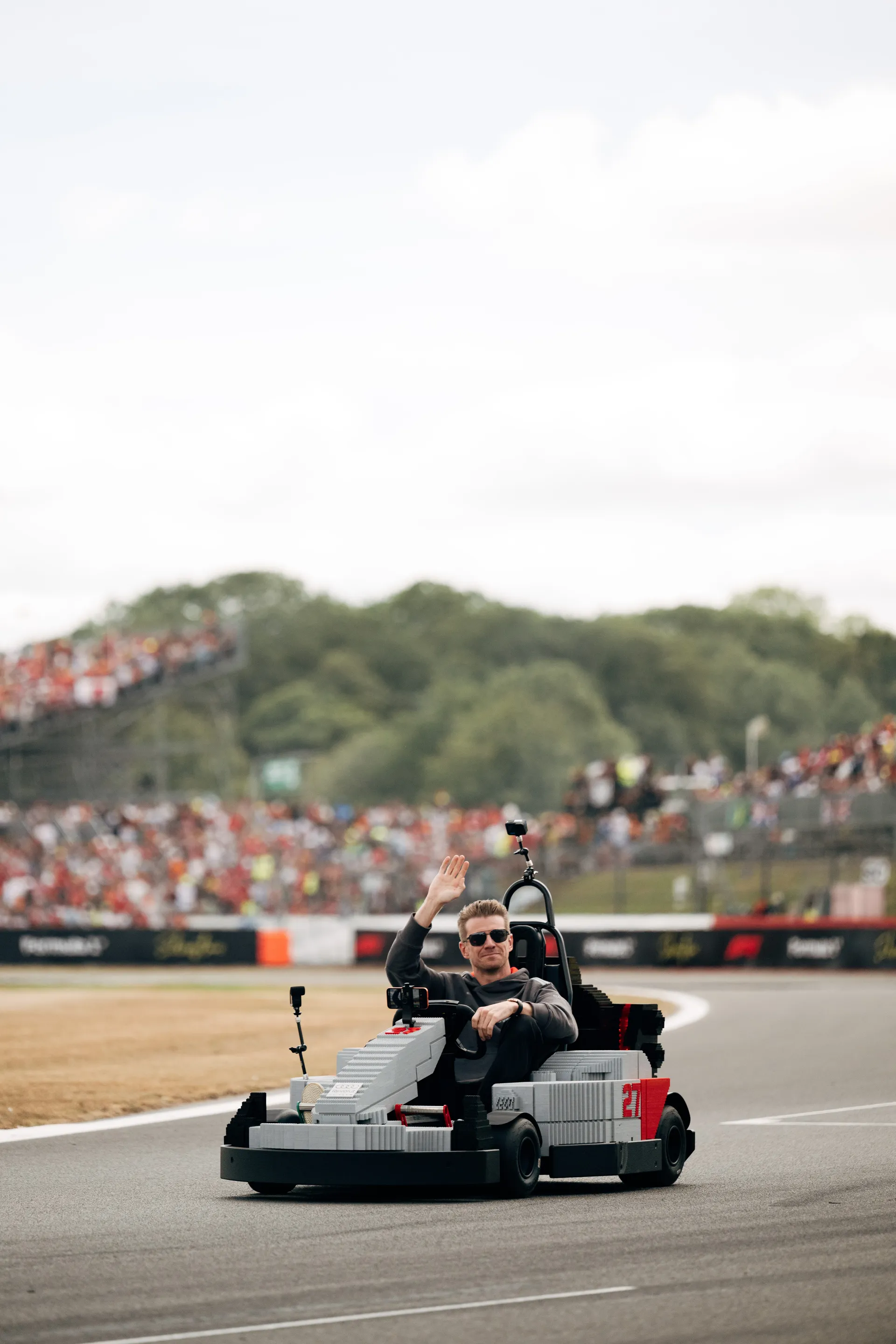 Nico Hulkenberg driving a LEGO® Audi R26 kart during the Drivers’ Parade, raising his hand to the crowd at Silverstone.