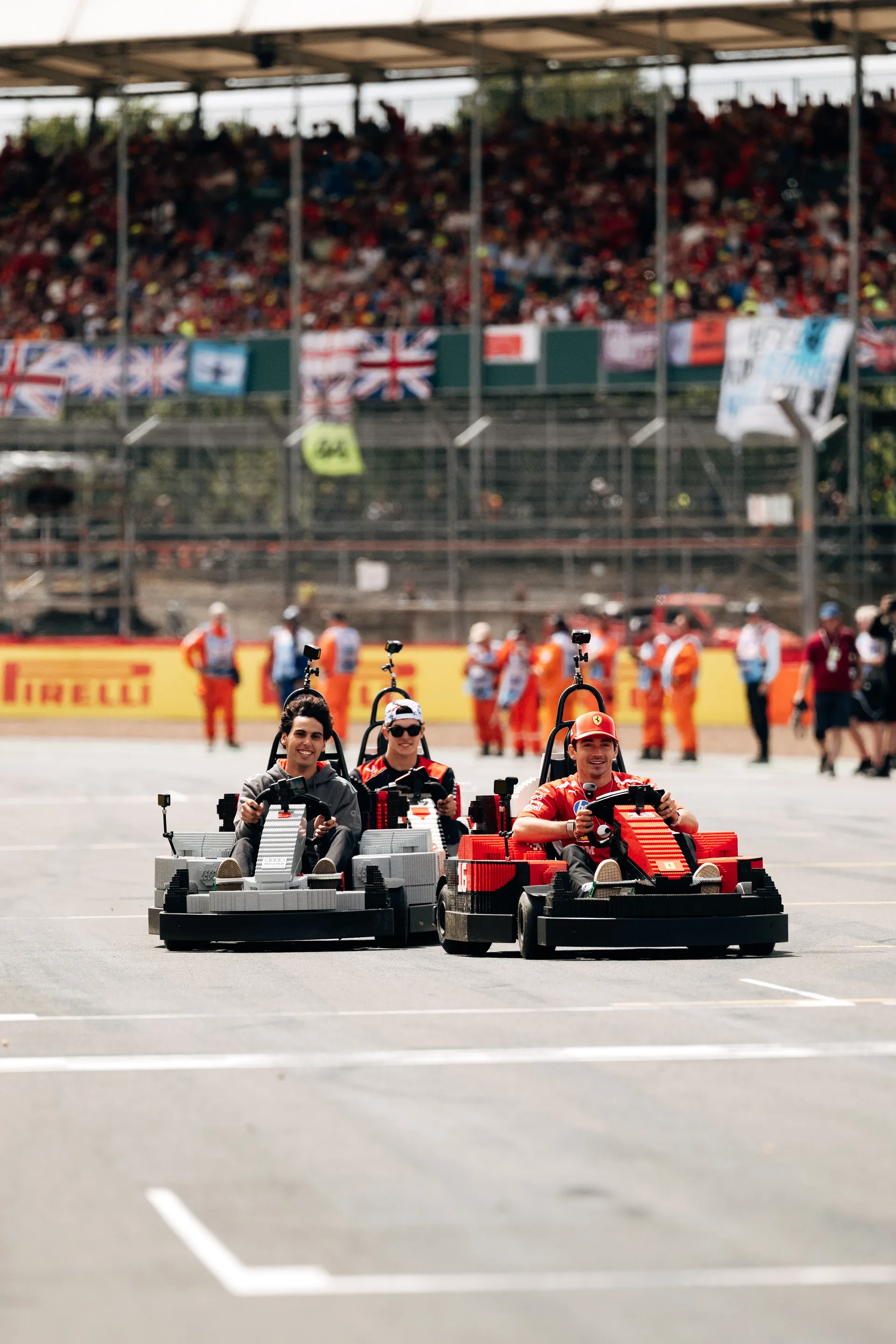 Three drivers racing LEGO® karts side by side during the Drivers’ Parade at Silverstone, with grandstands full of spectators in the background.