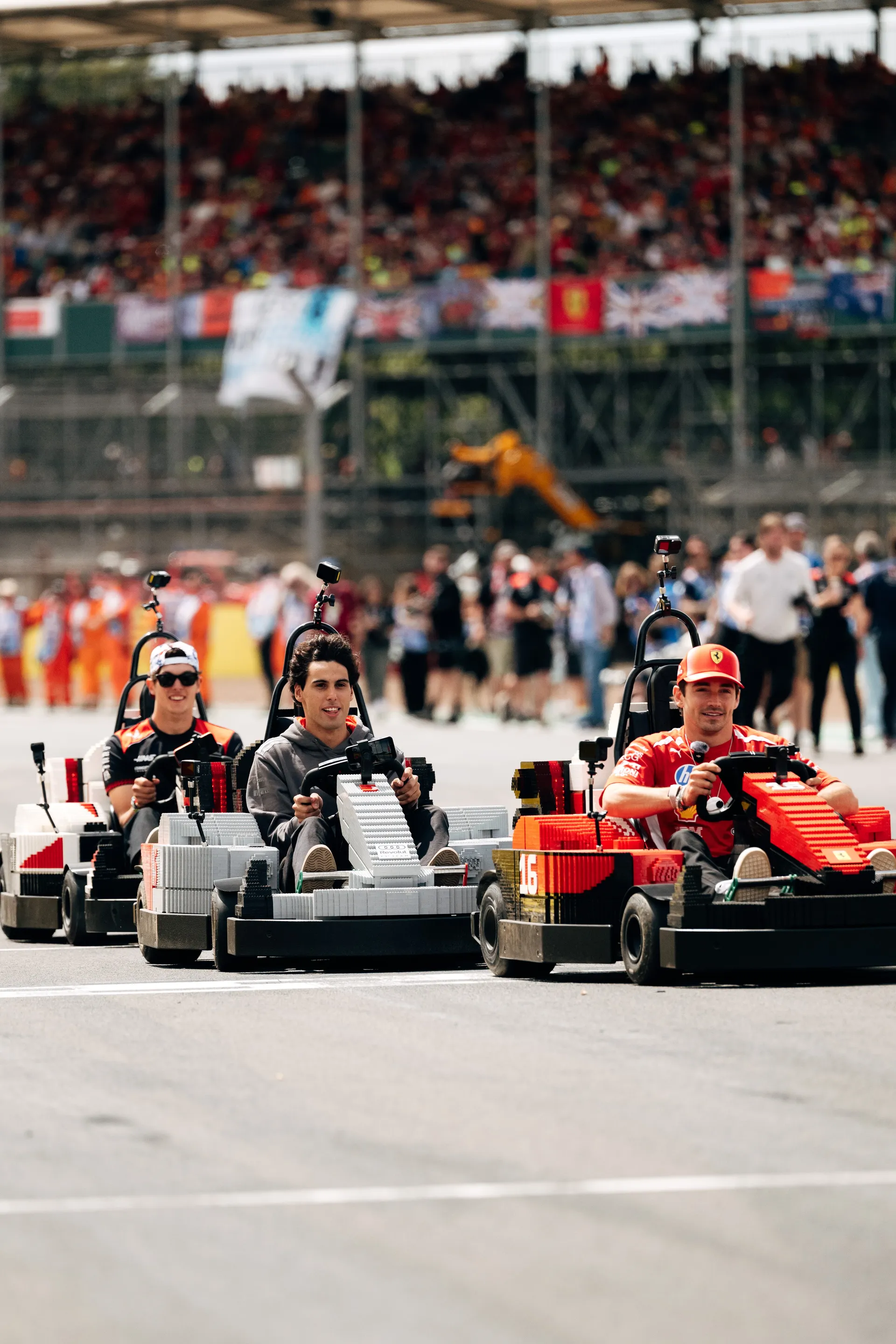 Three drivers racing LEGO® karts side by side during the Drivers’ Parade at Silverstone, with grandstands full of spectators in the background.