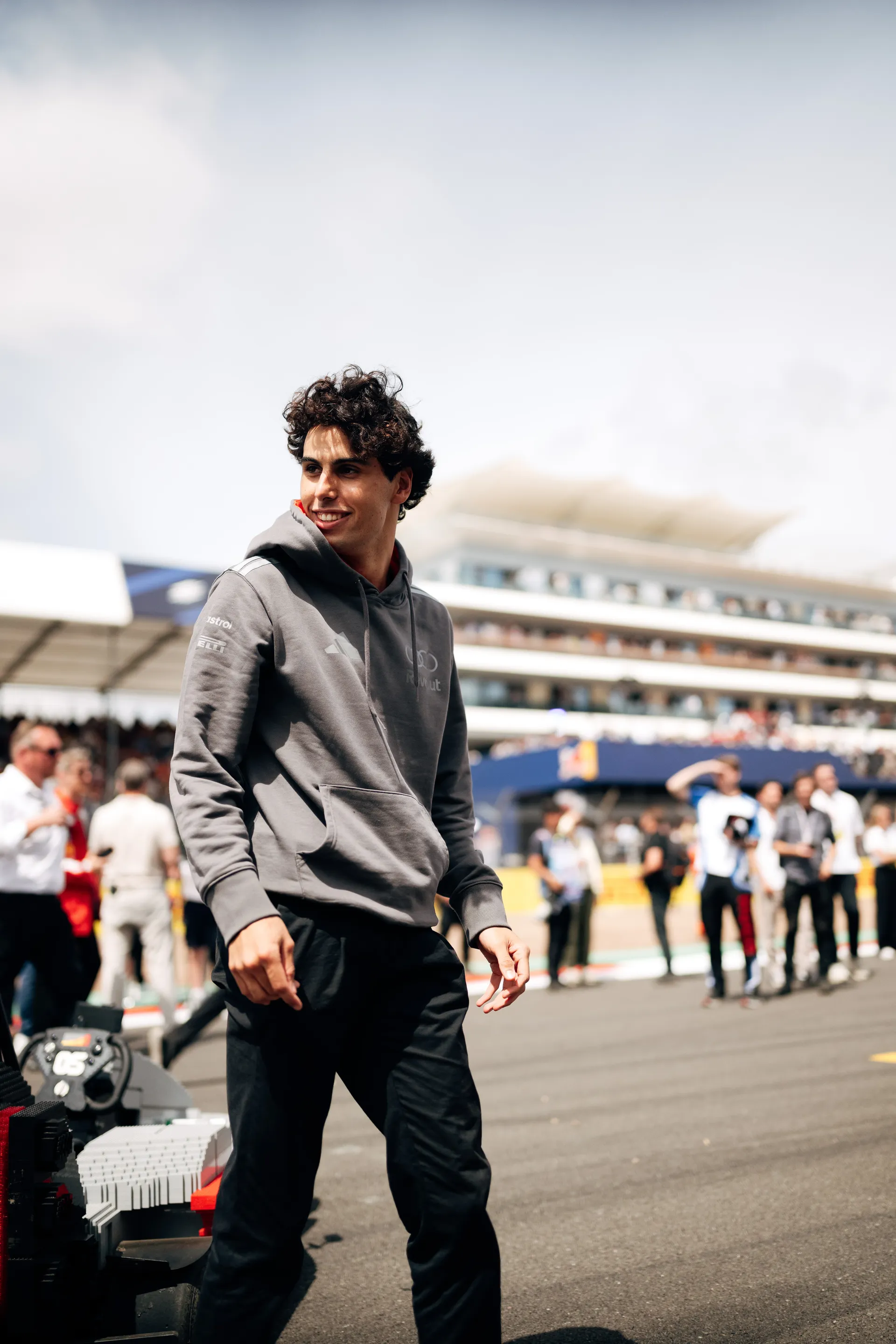 Gabriel Bortoleto walking past LEGO® Audi R26 karts in the paddock area at Silverstone, surrounded by team members and spectators.