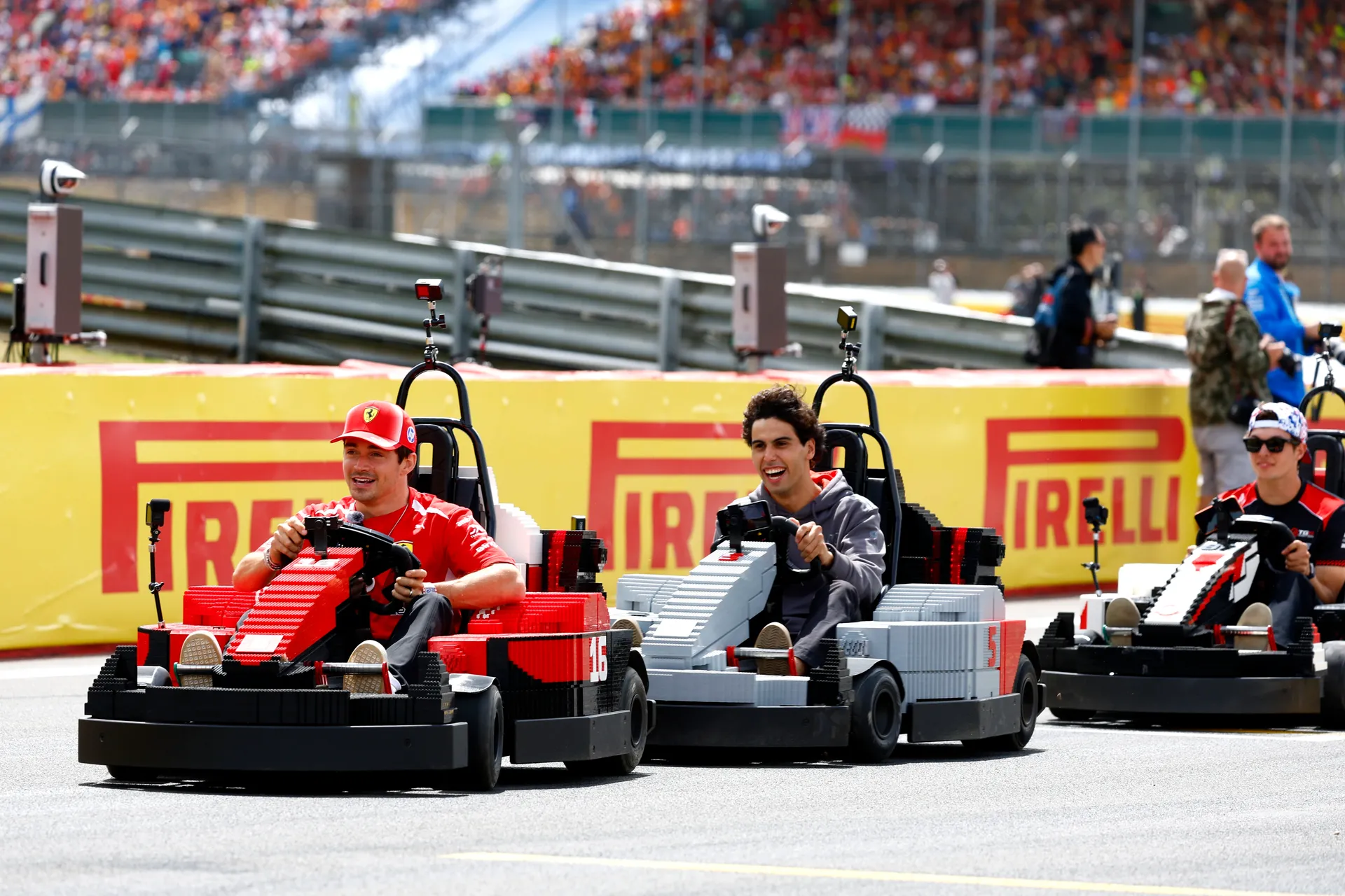 Charles Leclerc, Gabriel Bortoleto and another driver racing Audi R26 LEGO karts side by side in front of packed Silverstone grandstands.