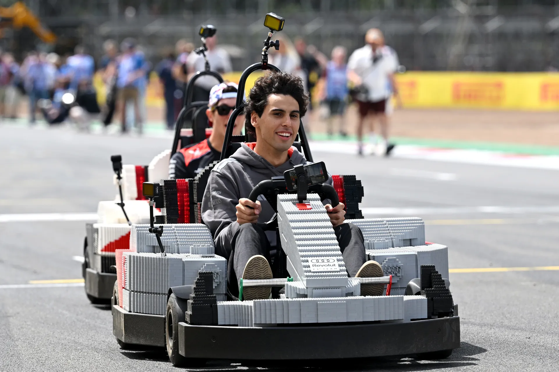 Gabriel Bortoleto driving an Audi R26 LEGO kart on the Silverstone circuit with another driver close behind.