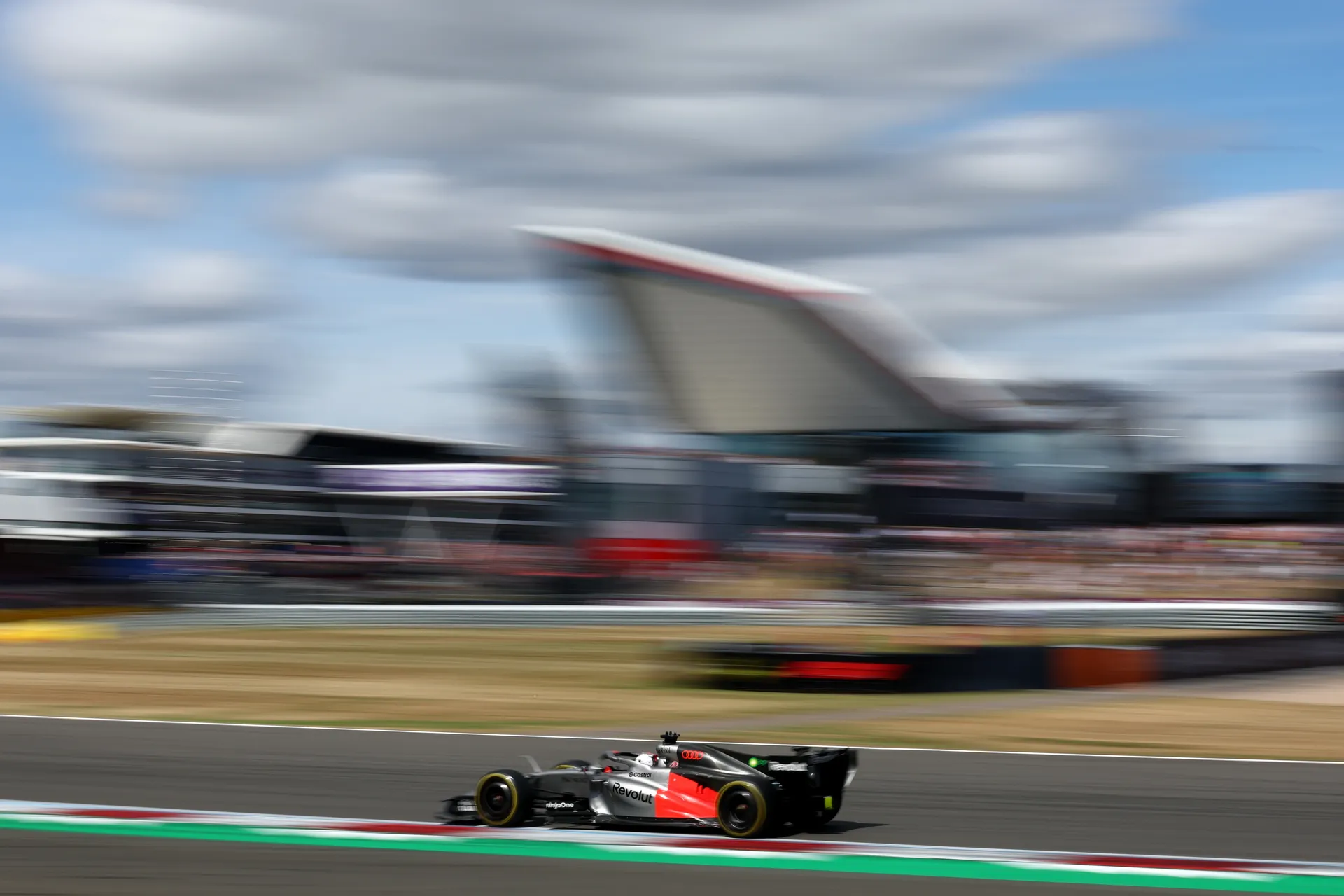 Audi R26 racing through a high-speed corner at Silverstone with blurred background.