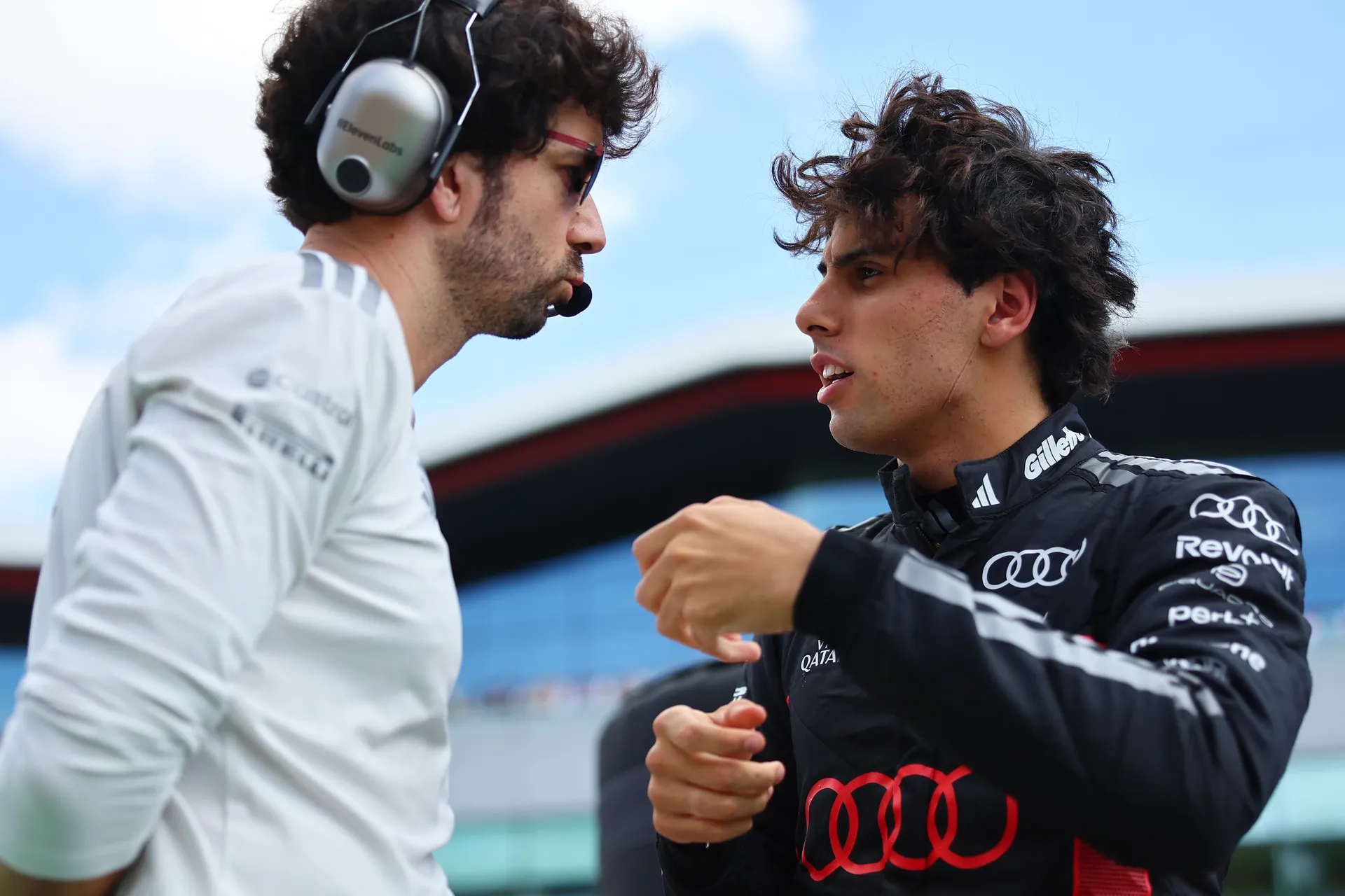 Gabriel Bortoleto in discussion with a race engineer on the grid, gesturing while receiving instructions.