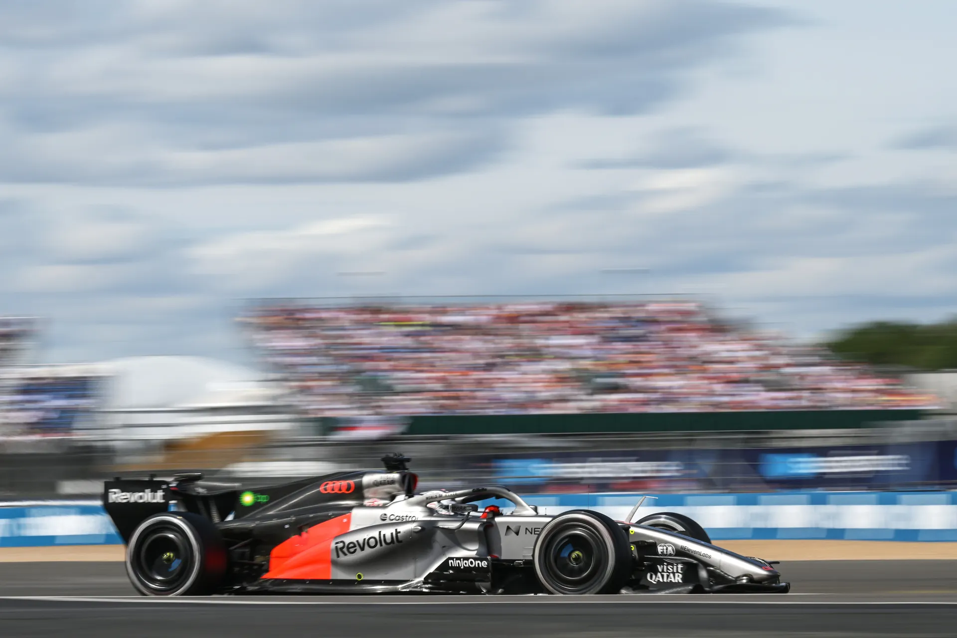 Audi R26 racing at speed along the Silverstone circuit with motion blur emphasising pace.