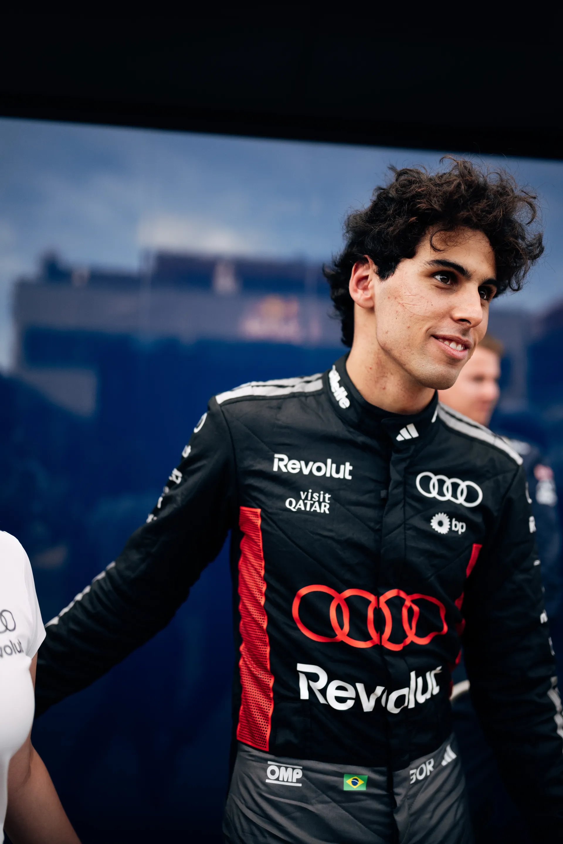 Gabriel Bortoleto stands in the paddock in his Audi Revolut F1® Team race suit, looking to the side with a focused and composed expression ahead of track action.