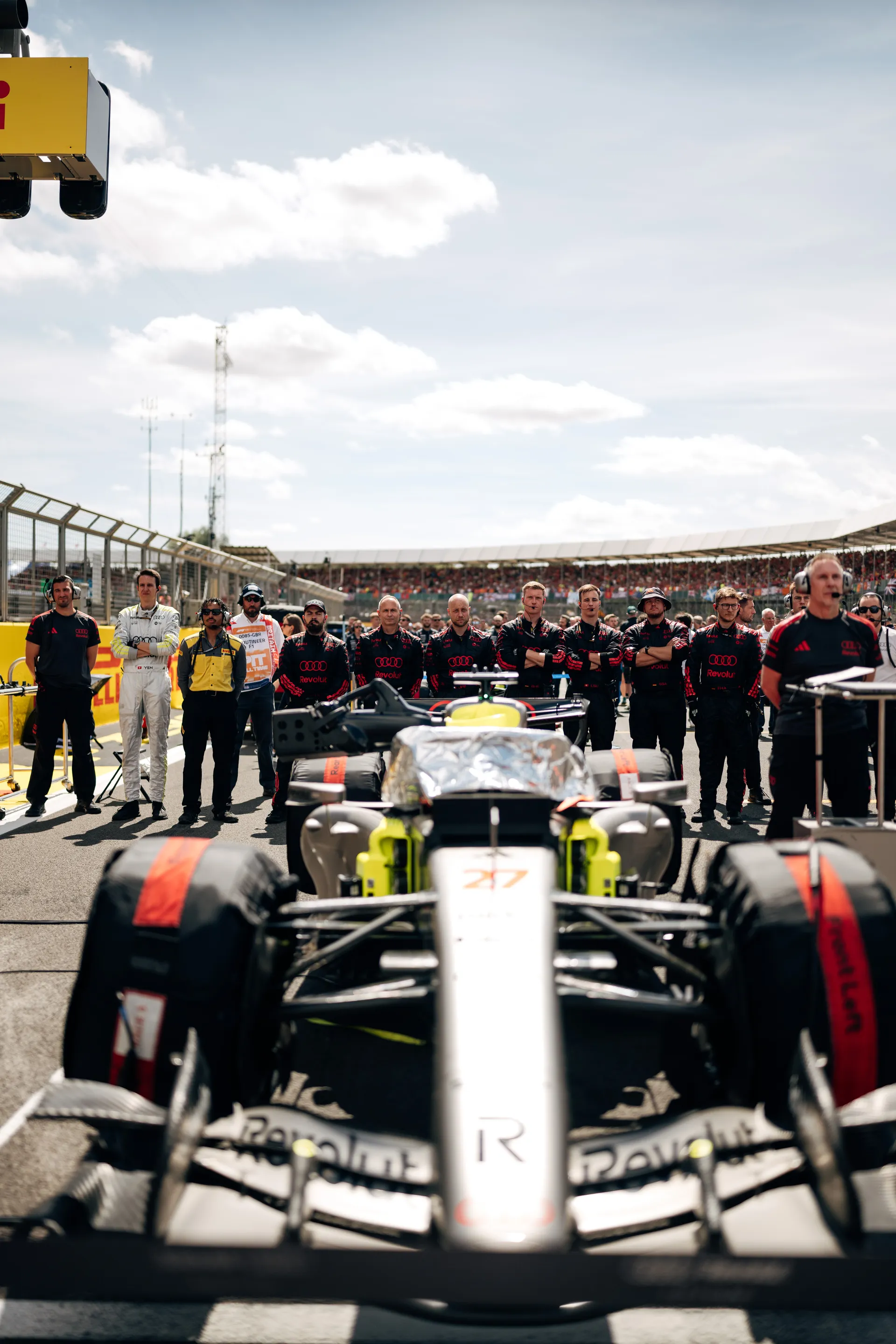 The Audi Revolut F1® Team lines up behind the R26 on the starting grid at Silverstone, focused on the car ahead of the race start.