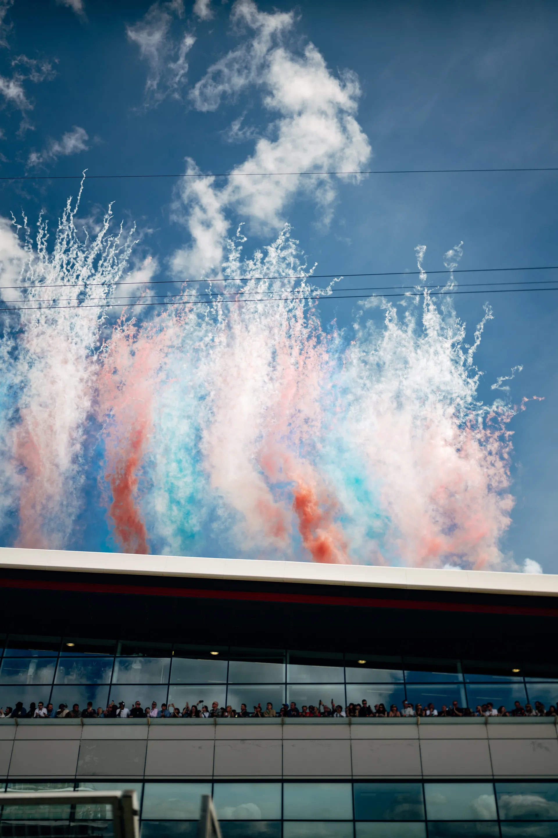 Red, white and blue smoke rises above the Silverstone grandstand while spectators watch from the building below.