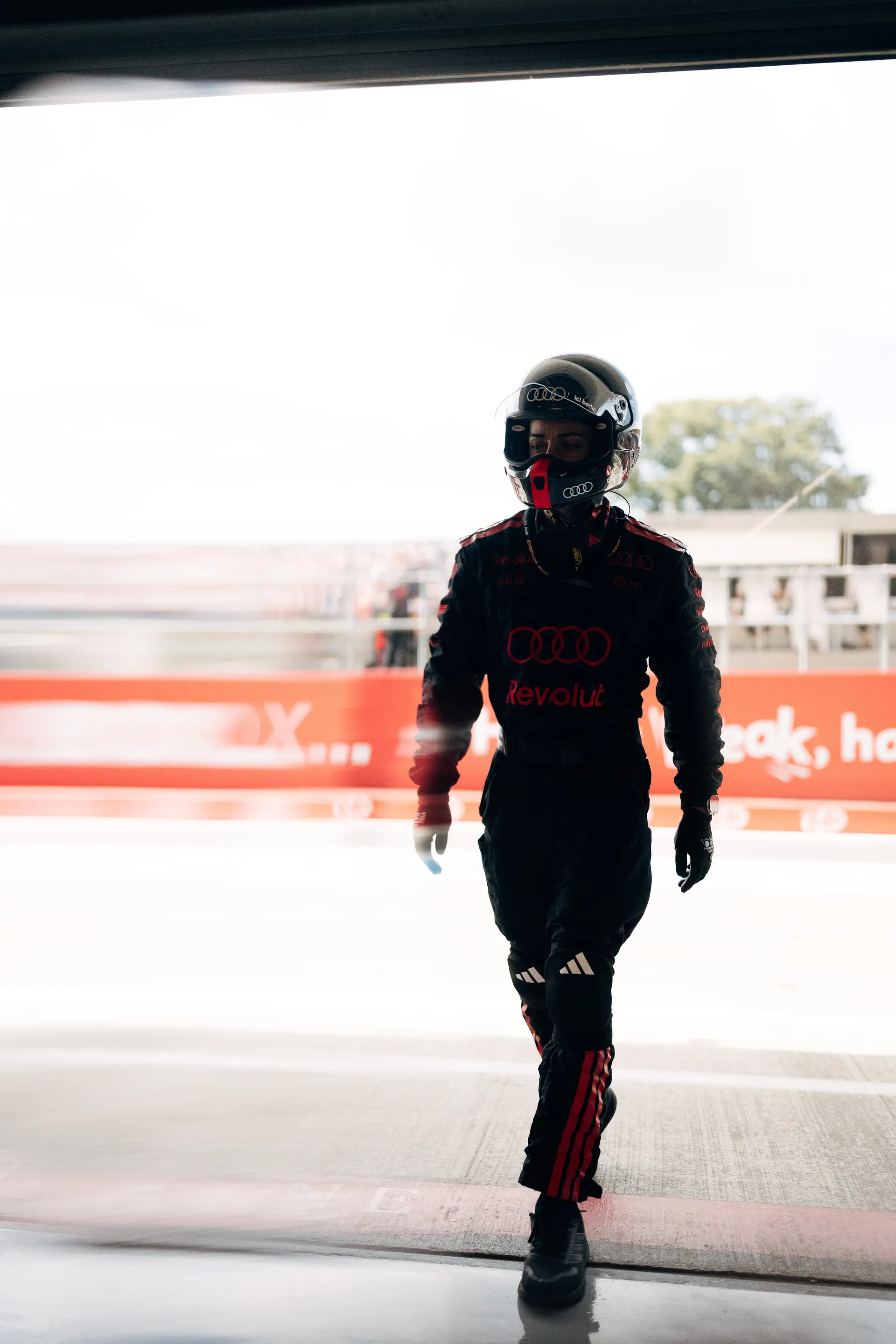 A crew member in full gear and helmet walks out of the garage towards the pit lane during race operations.