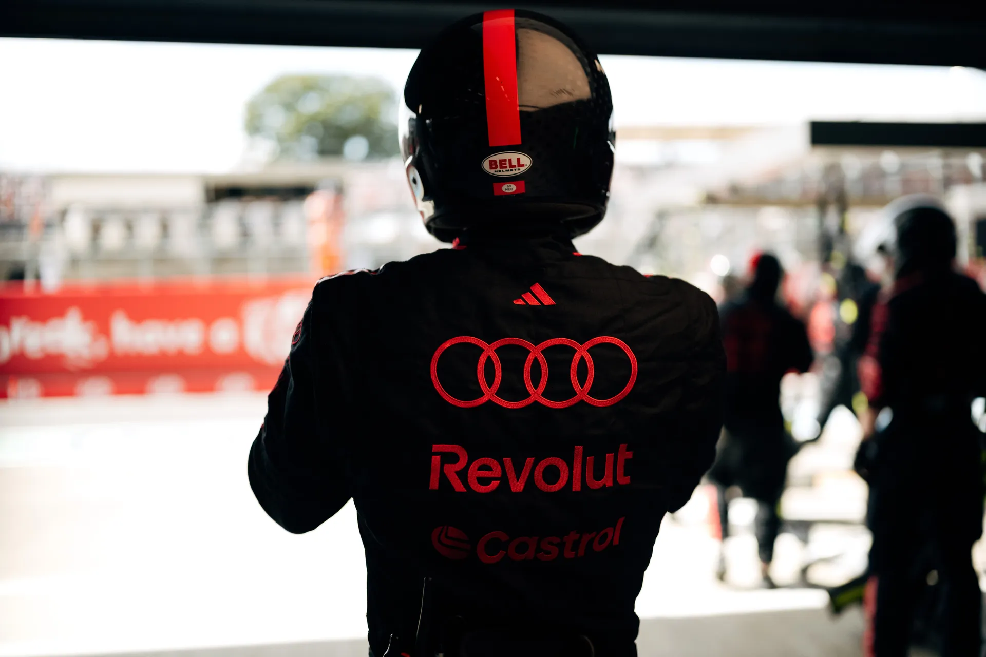 Rear view of an Audi Revolut F1® Team crew member shows Audi rings and sponsor logos on the race suit while heading towards the pit lane.