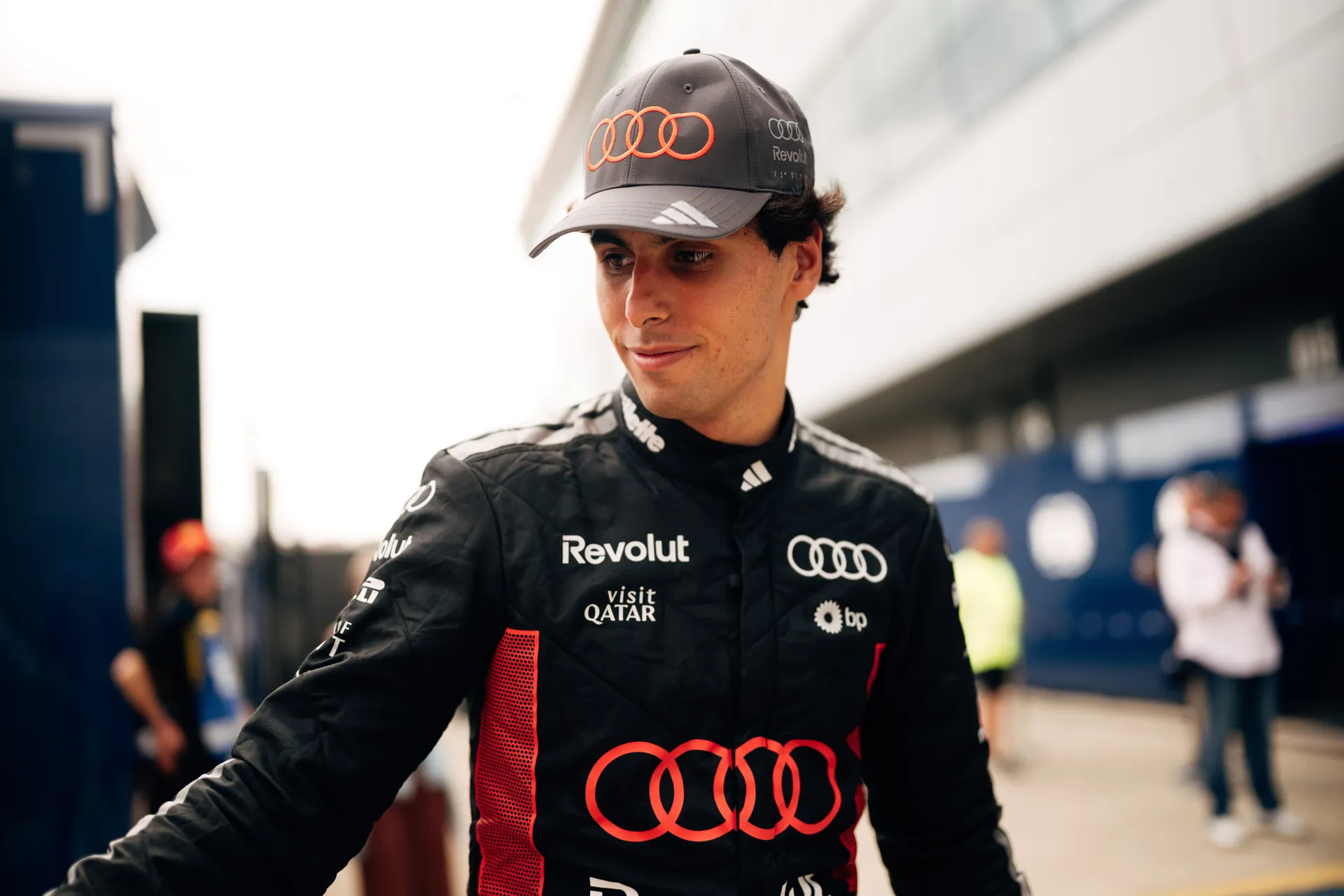 Gabriel Bortoleto adjusts his gloves beside the garage, wearing a team cap and preparing for the session.