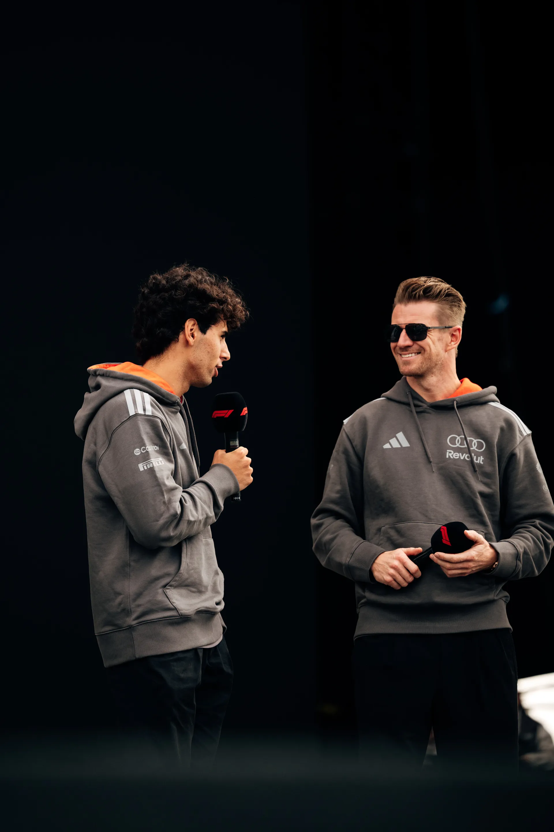 Gabriel Bortoleto speaking into a microphone while Nico Hulkenberg listens beside him on stage at Silverstone.