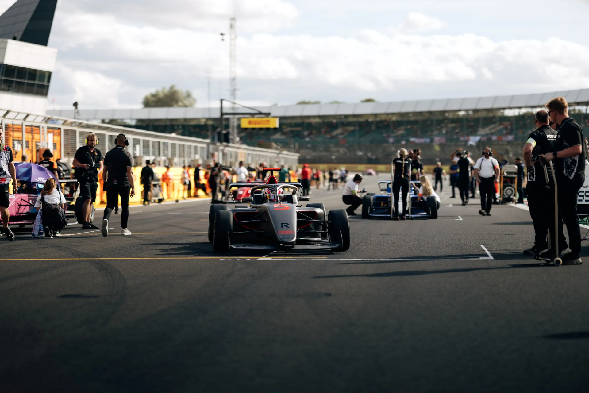 Audi R26 Formula One car positioned on the Silverstone grid surrounded by team members and other cars before the session.