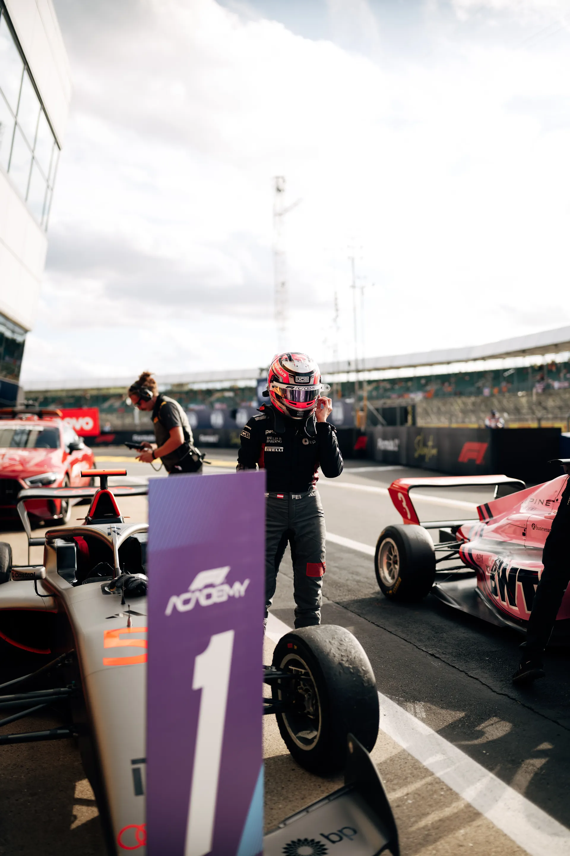 Emma Felbermayr standing beside her F1 Academy car on the Silverstone grid, adjusting her helmet before the session.