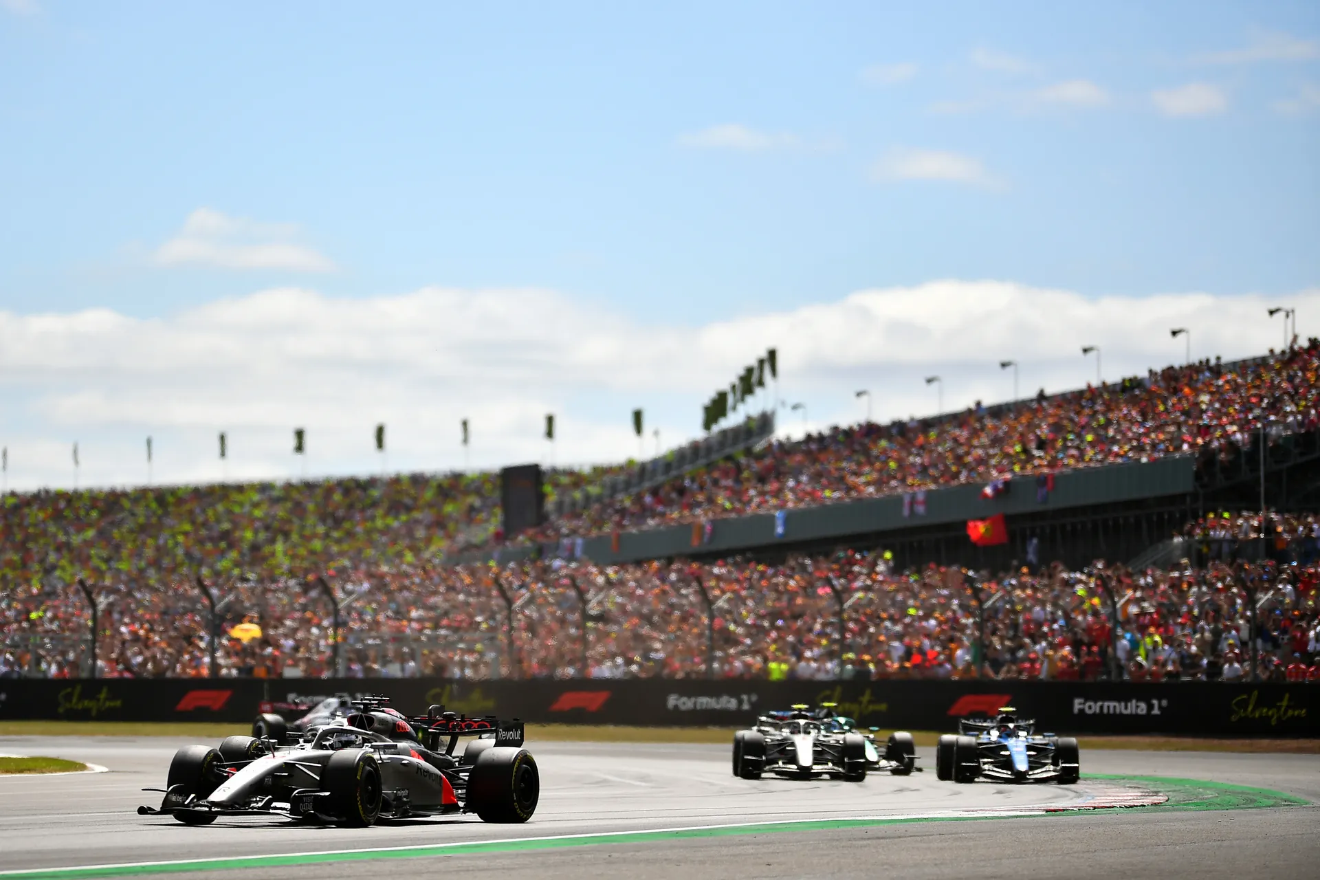 Audi Revolut F1® Team cars of Gabriel Bortoleto and Nico Hulkenberg competing through a corner in front of packed Silverstone grandstands.