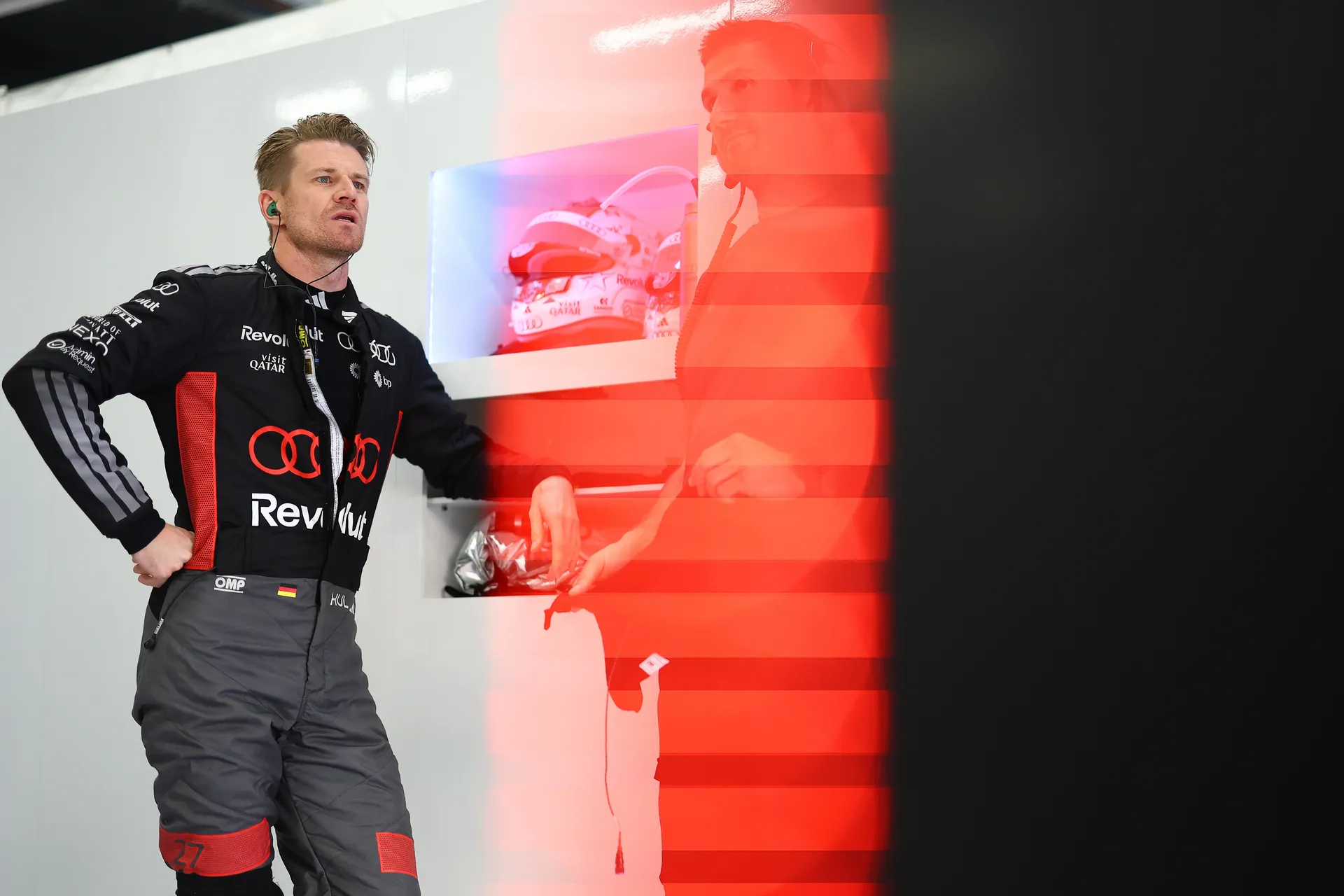 Nico Hulkenberg in the Audi Revolut F1® Team garage wearing race suit and earpiece while speaking with a team member.
